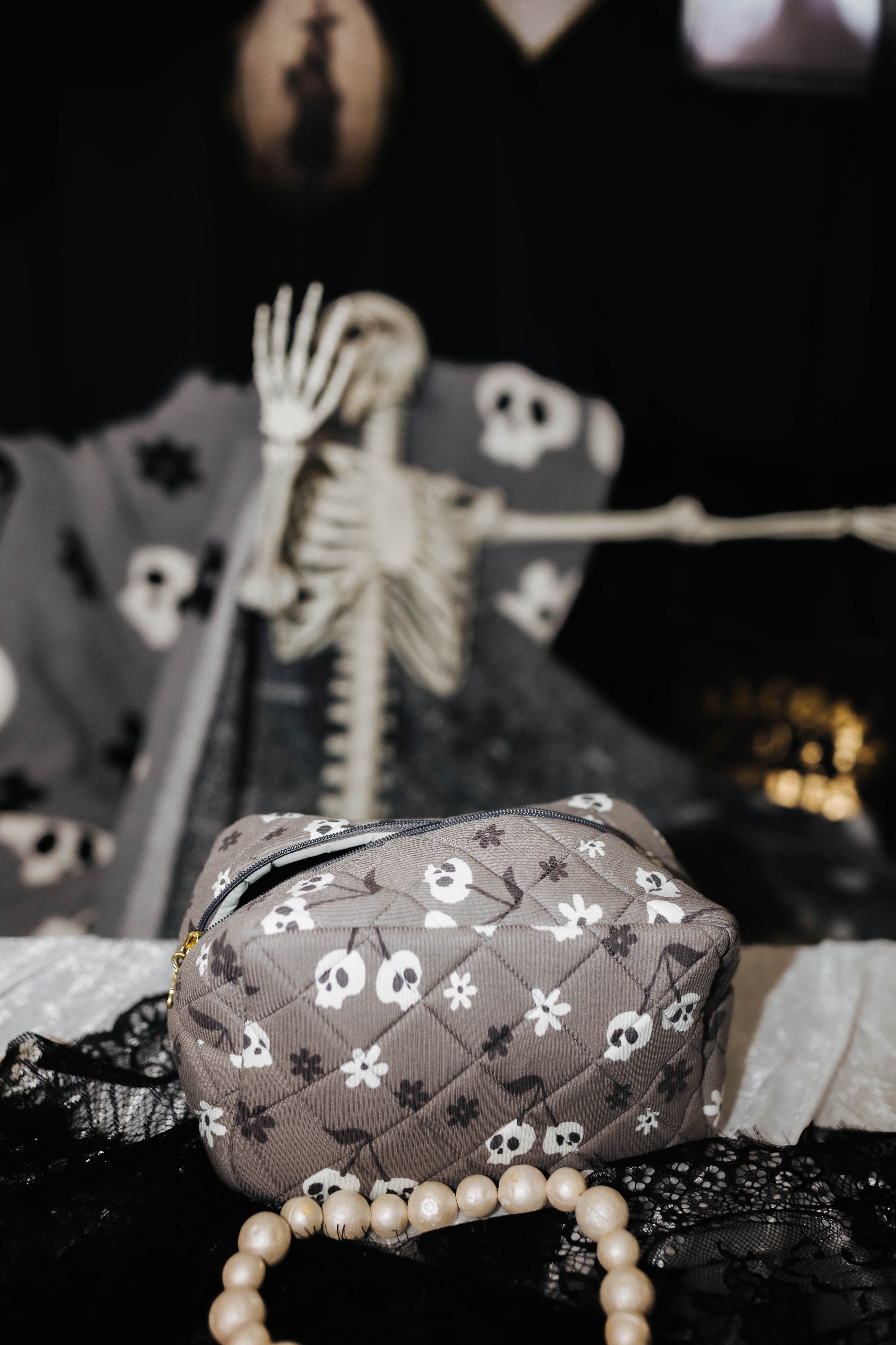 skelly cosmetic bag on table with spooky decorations in the background