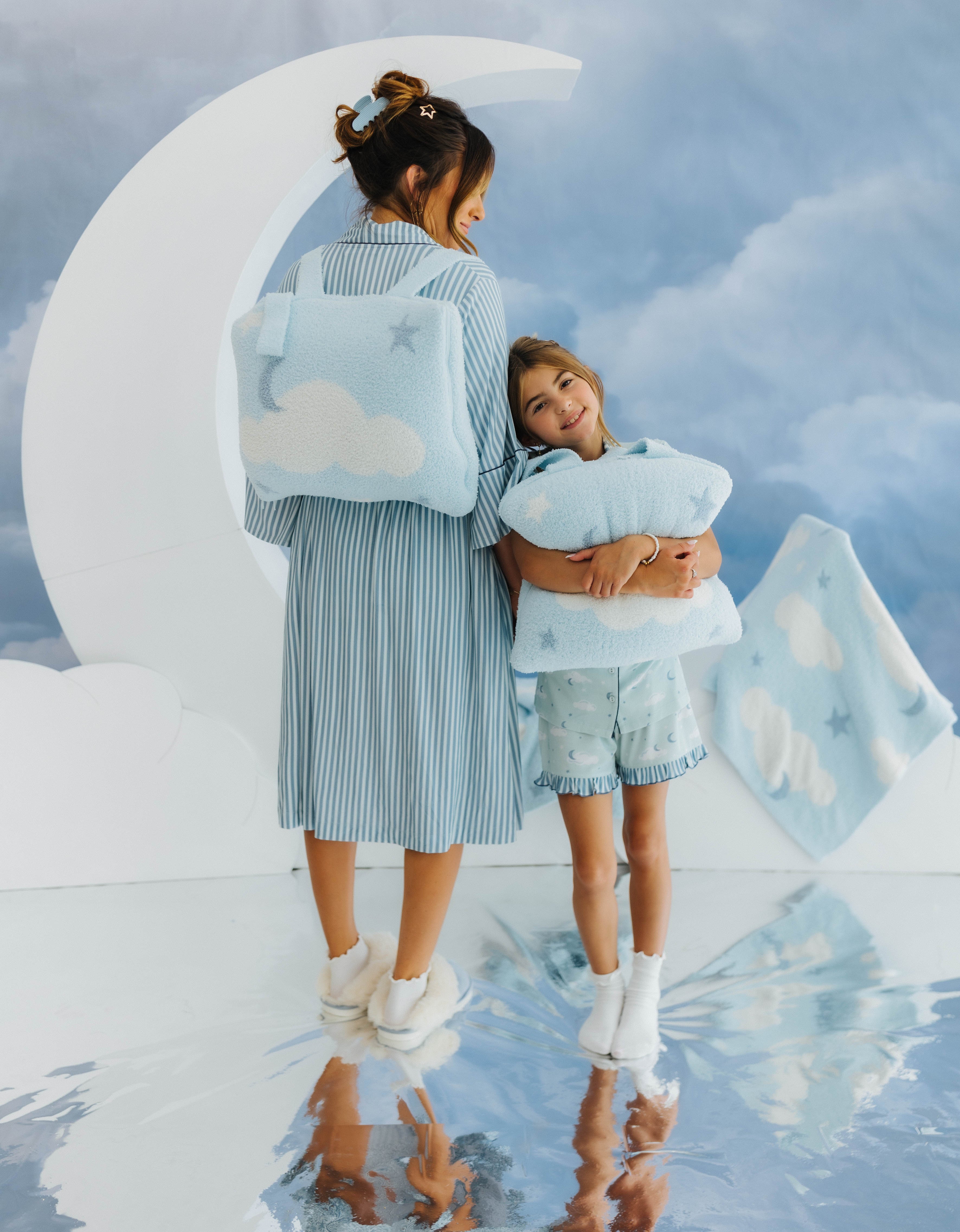 Two people in light blue outfits standing in front of a large moon and cloud decoration.