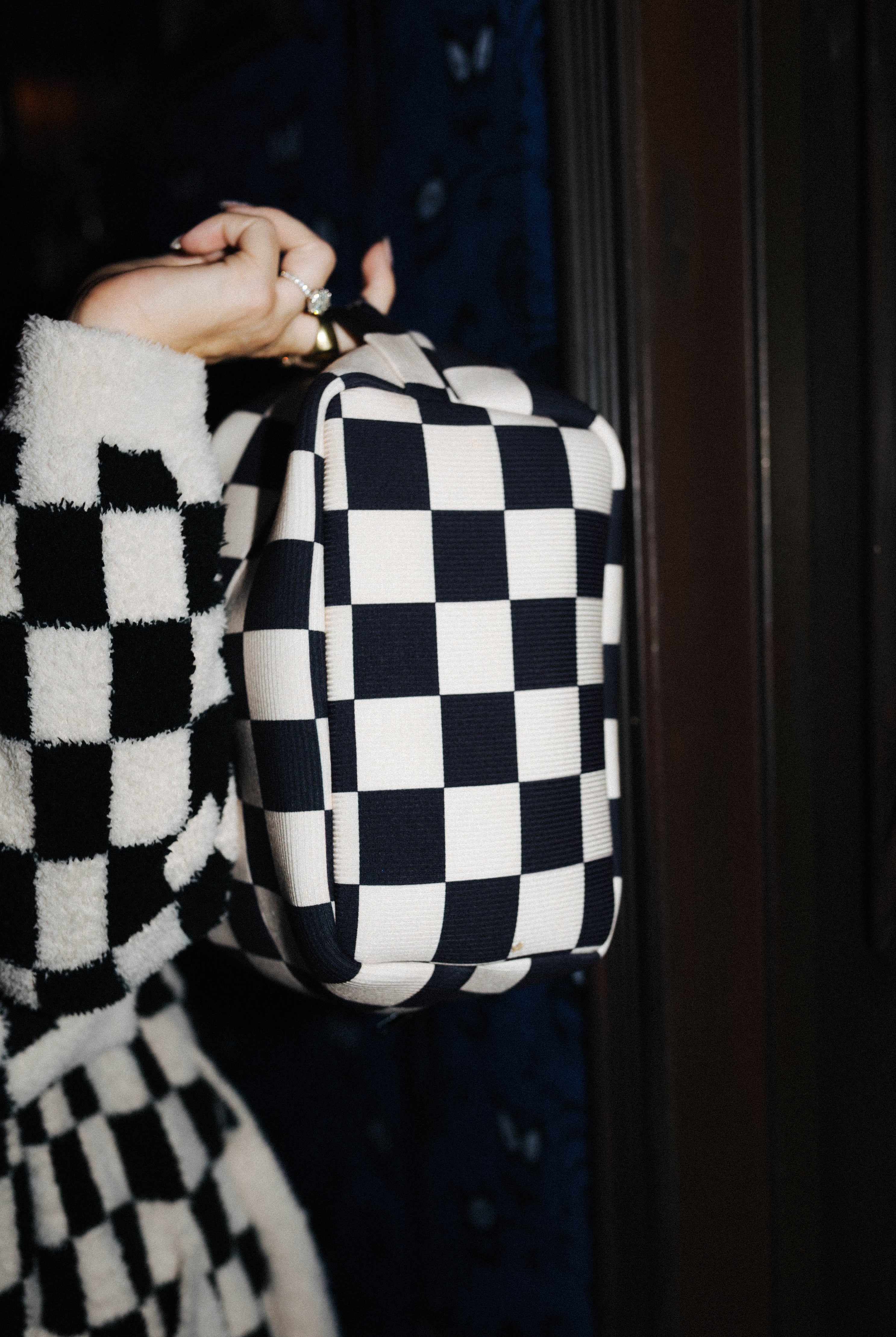 Sand and black check cosmetic bag shown from the side by its top handle