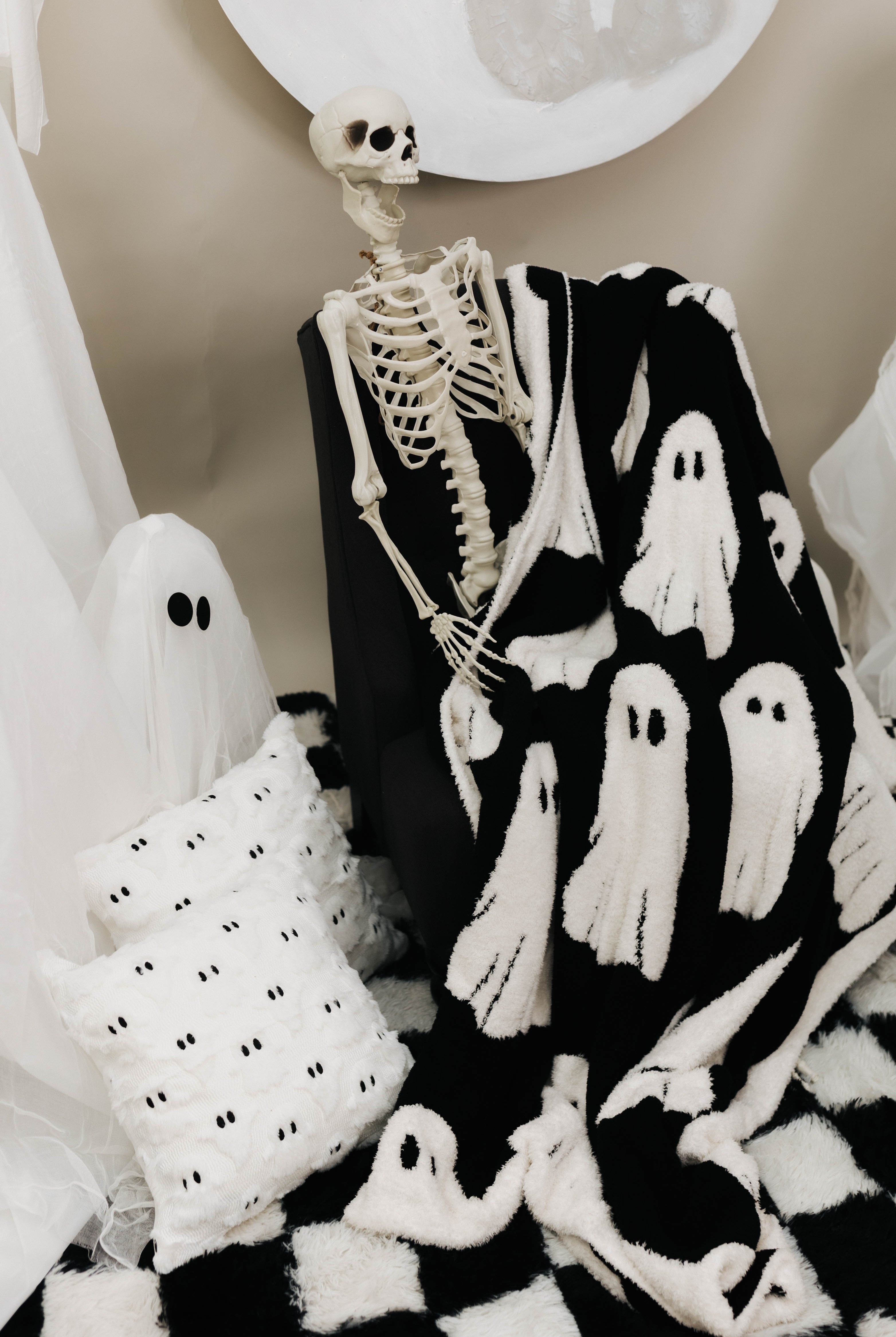 ghost blanket laying in lap of skeleton with ghost decorations in the back