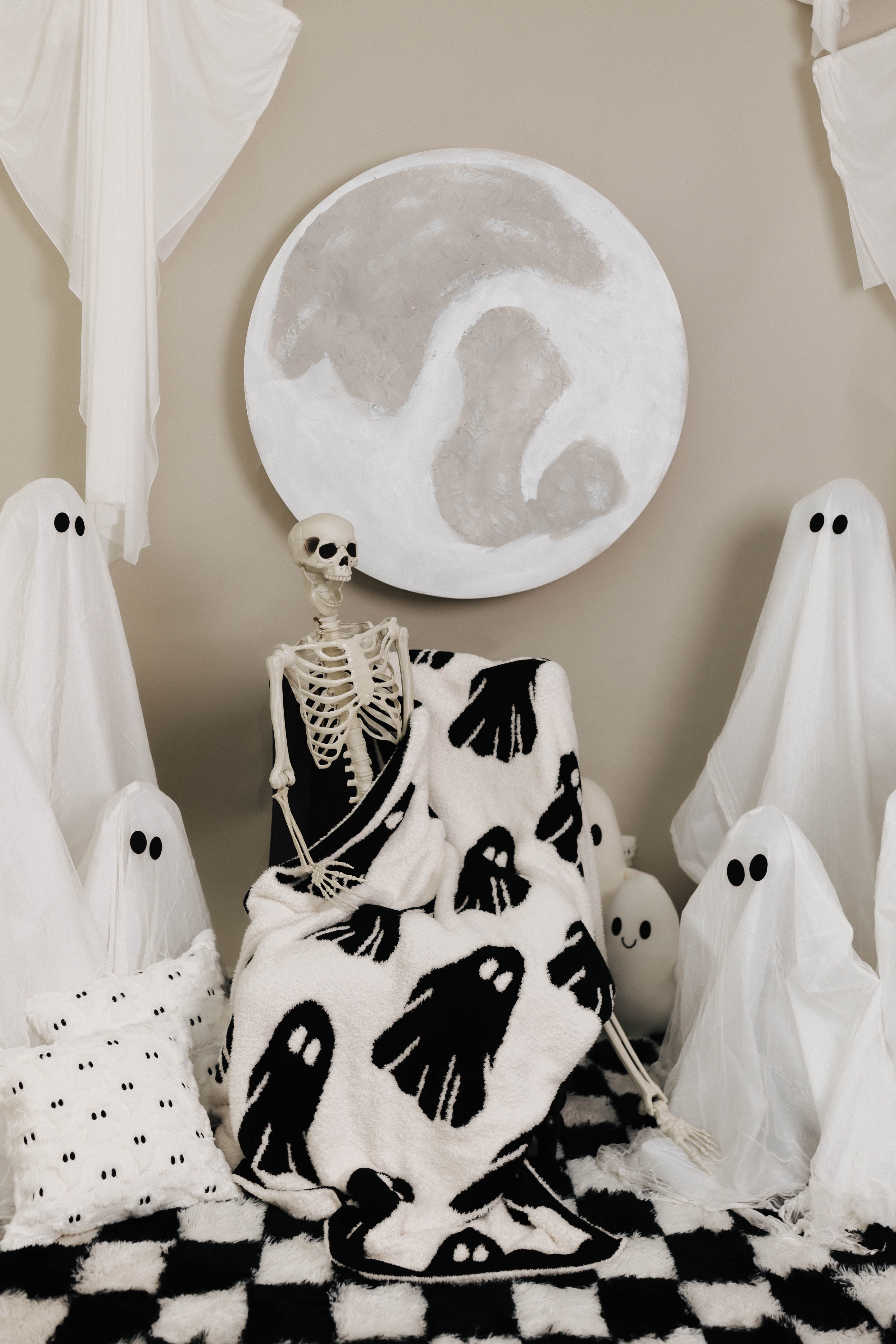 ghost blanket laying in the lap of skeleton with ghost decorations in the background