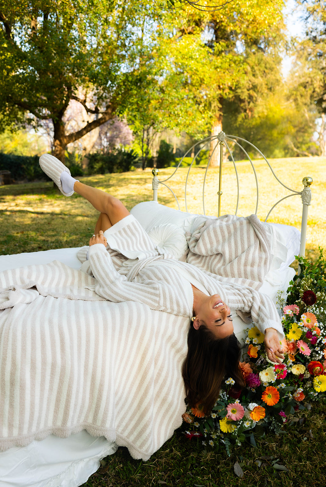 Woman lying on a bed outdoors with flowers and trees in the background