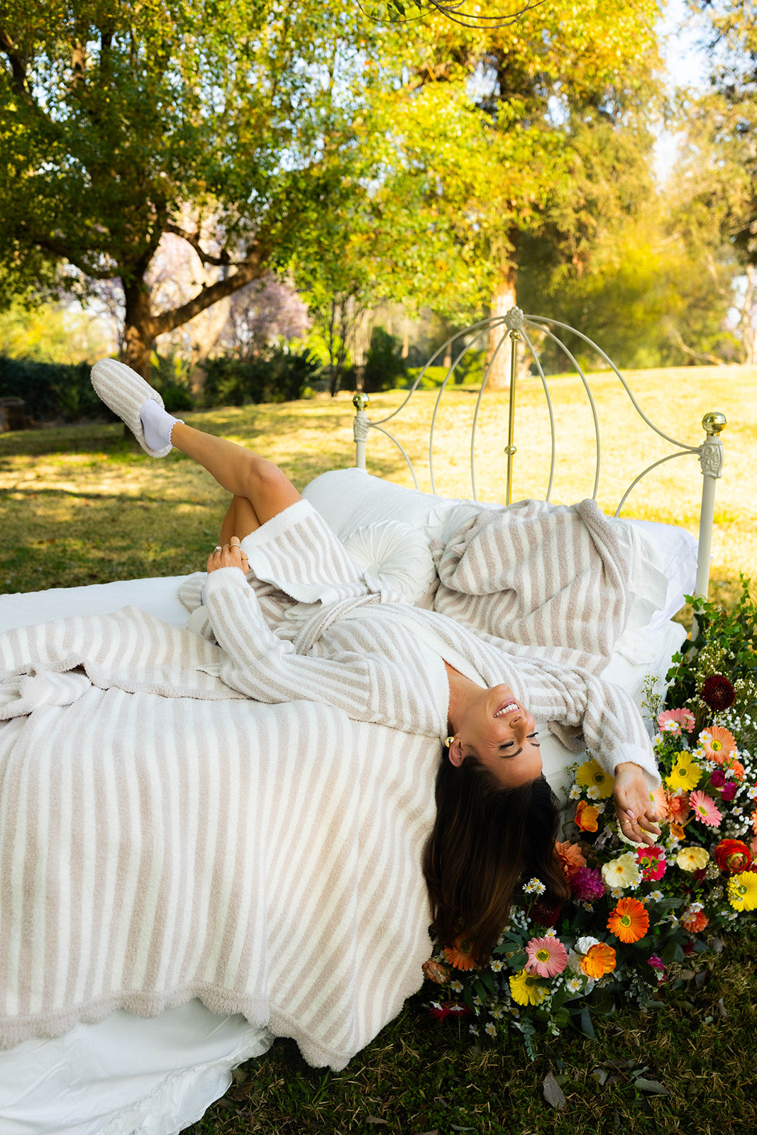 Woman lying on a bed outdoors with flowers and trees in the background
