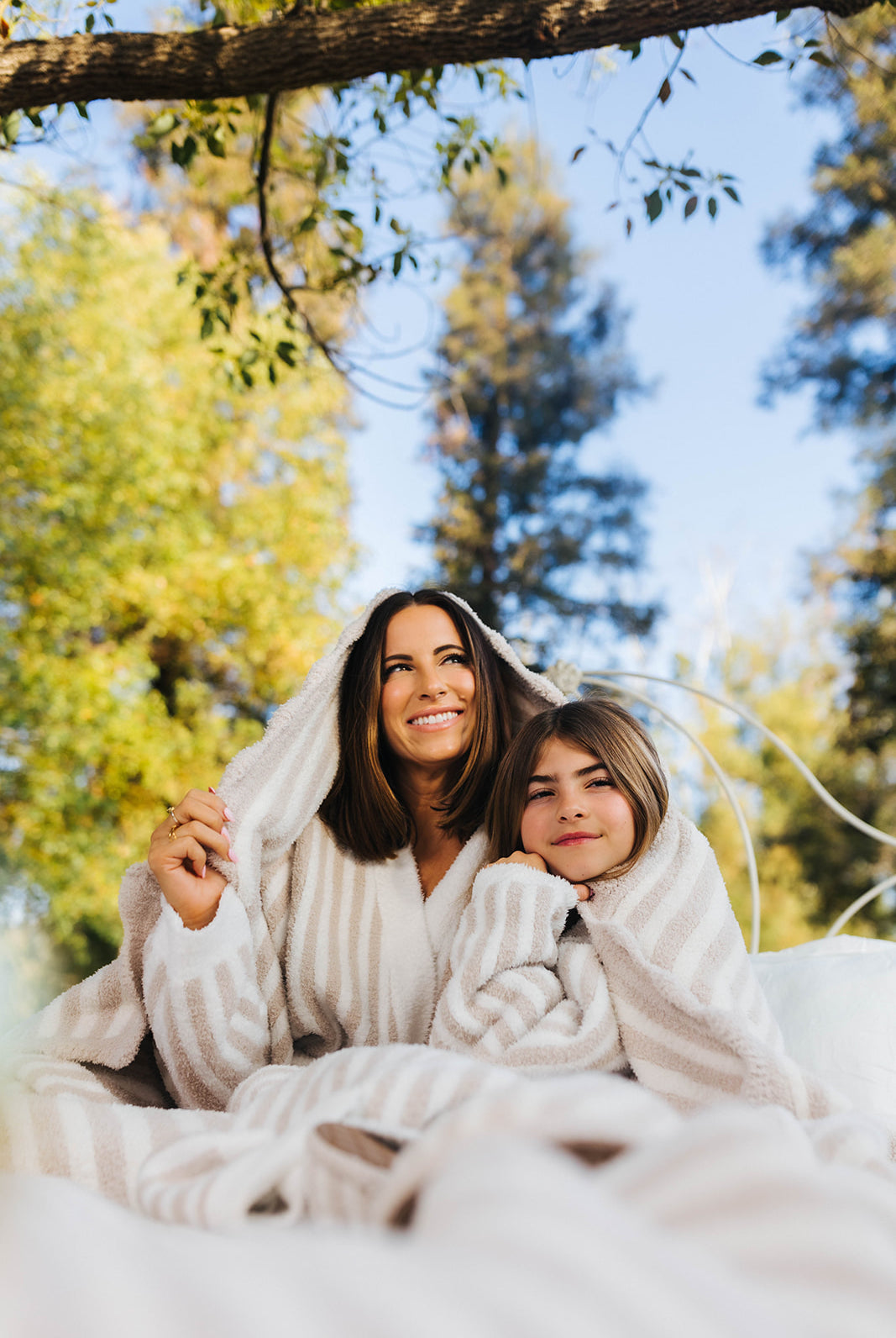Woman and child wrapped in a blanket outdoors with trees in the background