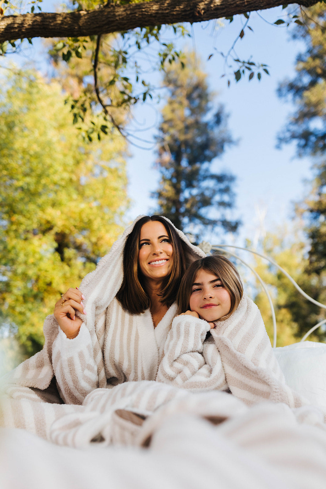 Woman and child wrapped in a blanket outdoors with trees in the background