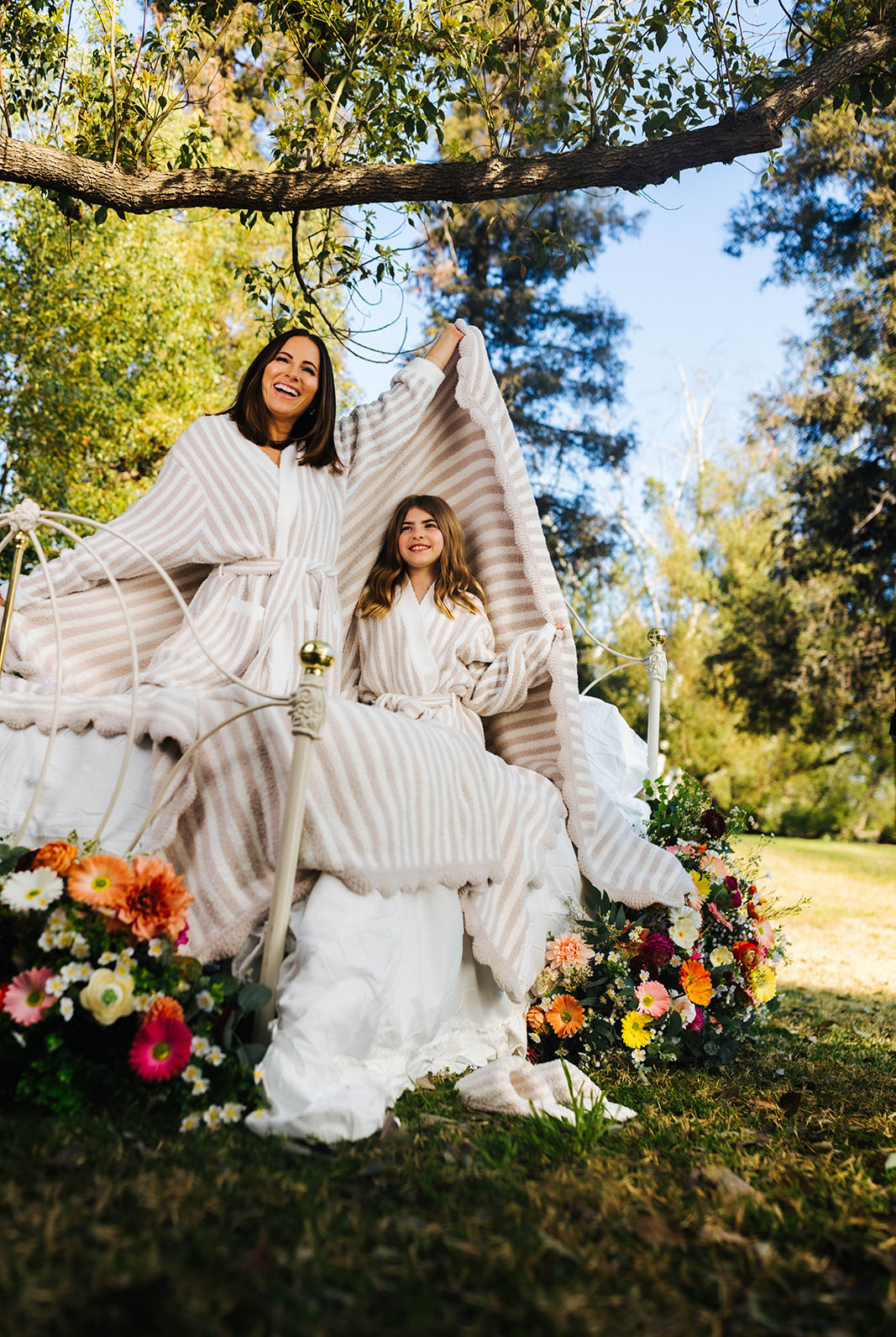 Two women in robes sitting under a tree with flowers around them.
