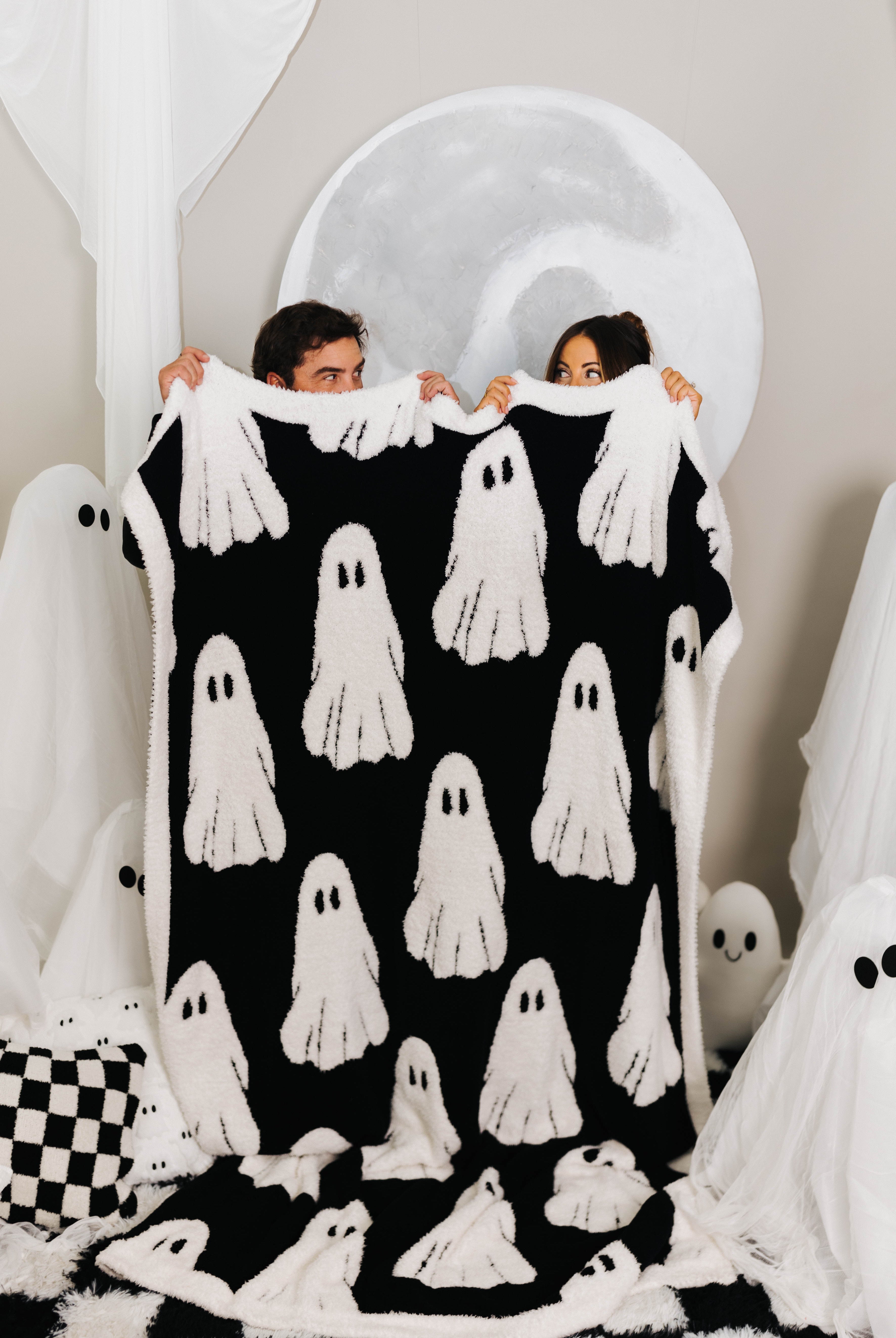 two people holding host blanket showing the black and white ghosts with ghosts decorations in the back