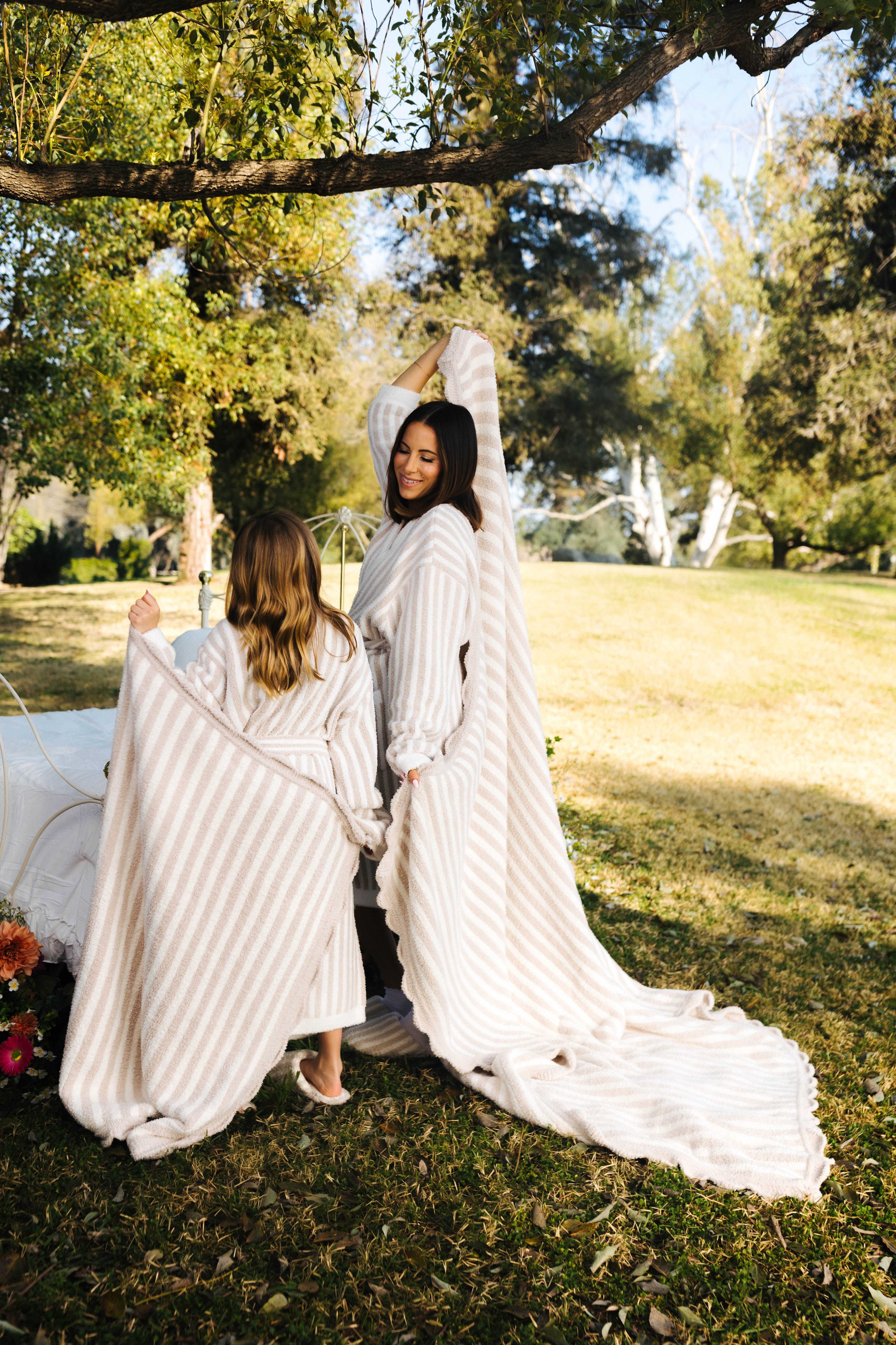 Krista and Kolly holding up the pinstripe blankets in front of trees