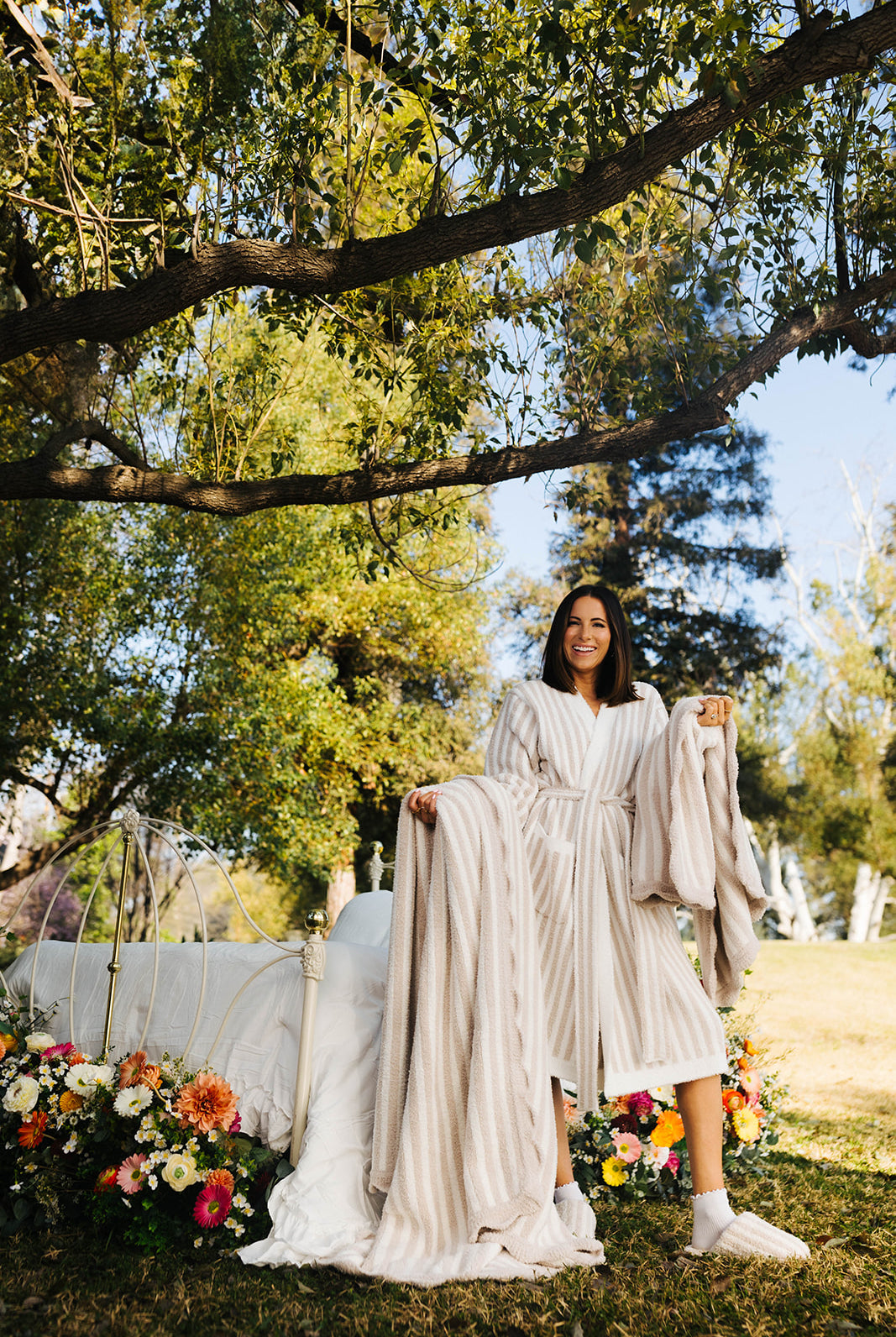 Woman in a pinstripe robe standing outdoors with trees and flowers in the background