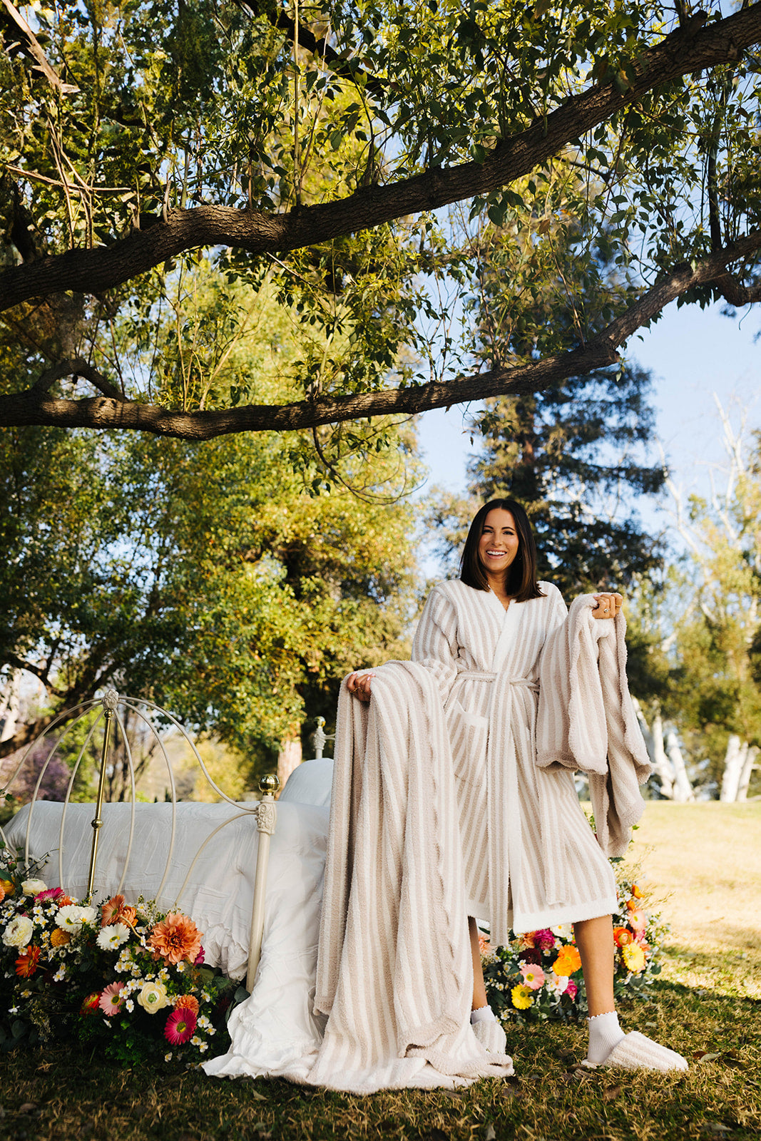 Woman in a pinstripe robe standing outdoors with trees and flowers in the background