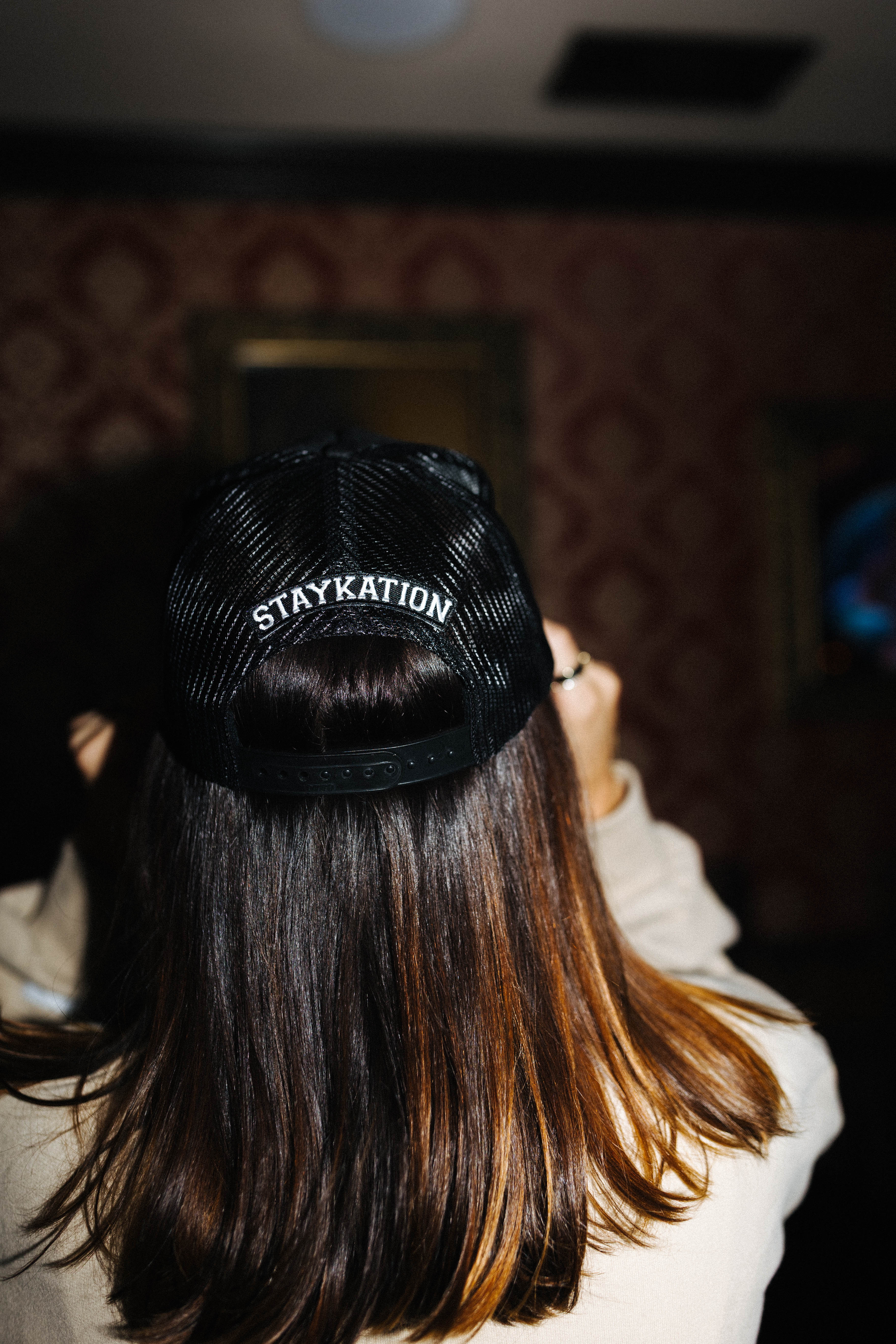 Back view of the black Hot Mess trucker hat with Staykation lettering