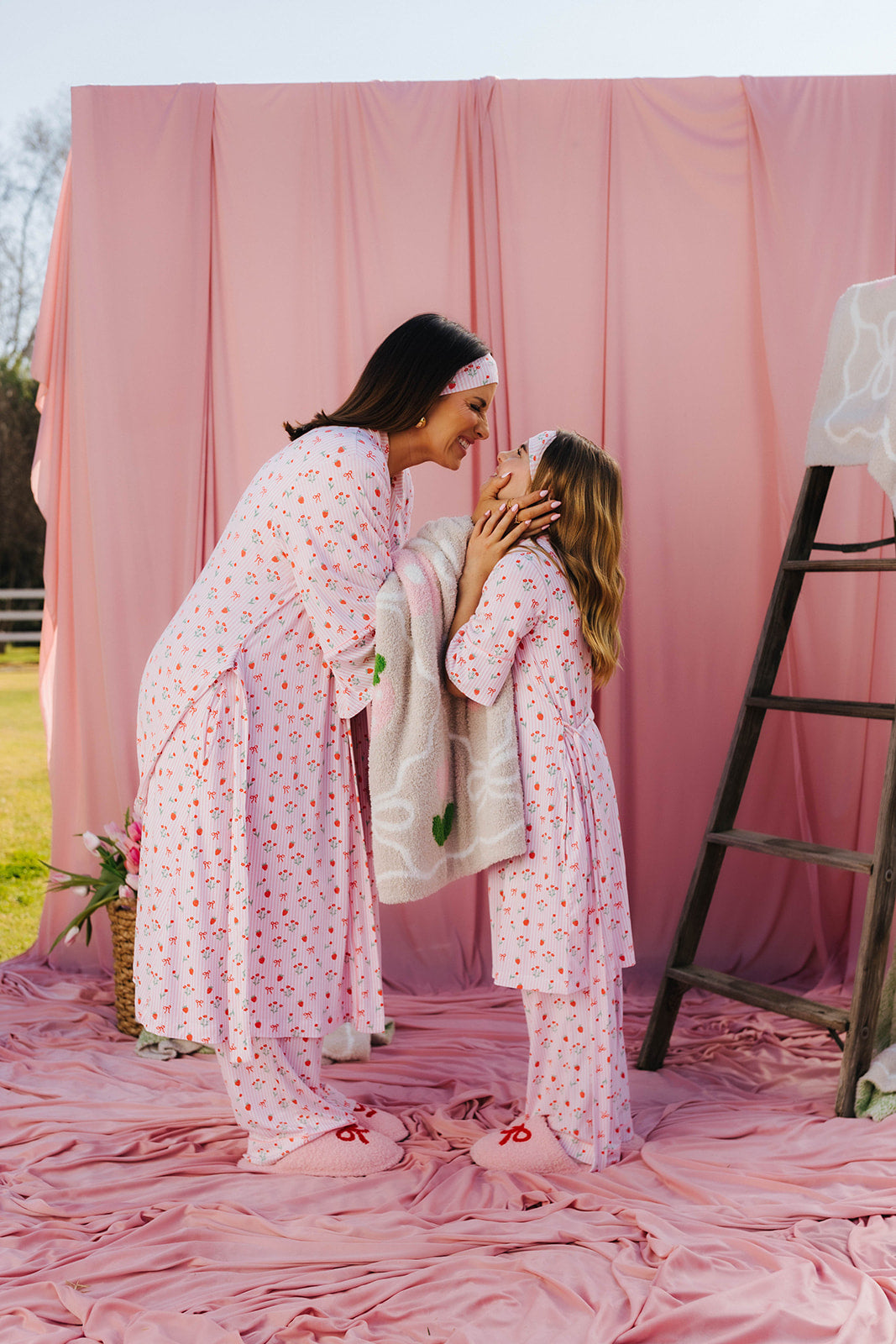 Woman and child in matching pink outfits standing on a pink fabric backdrop.