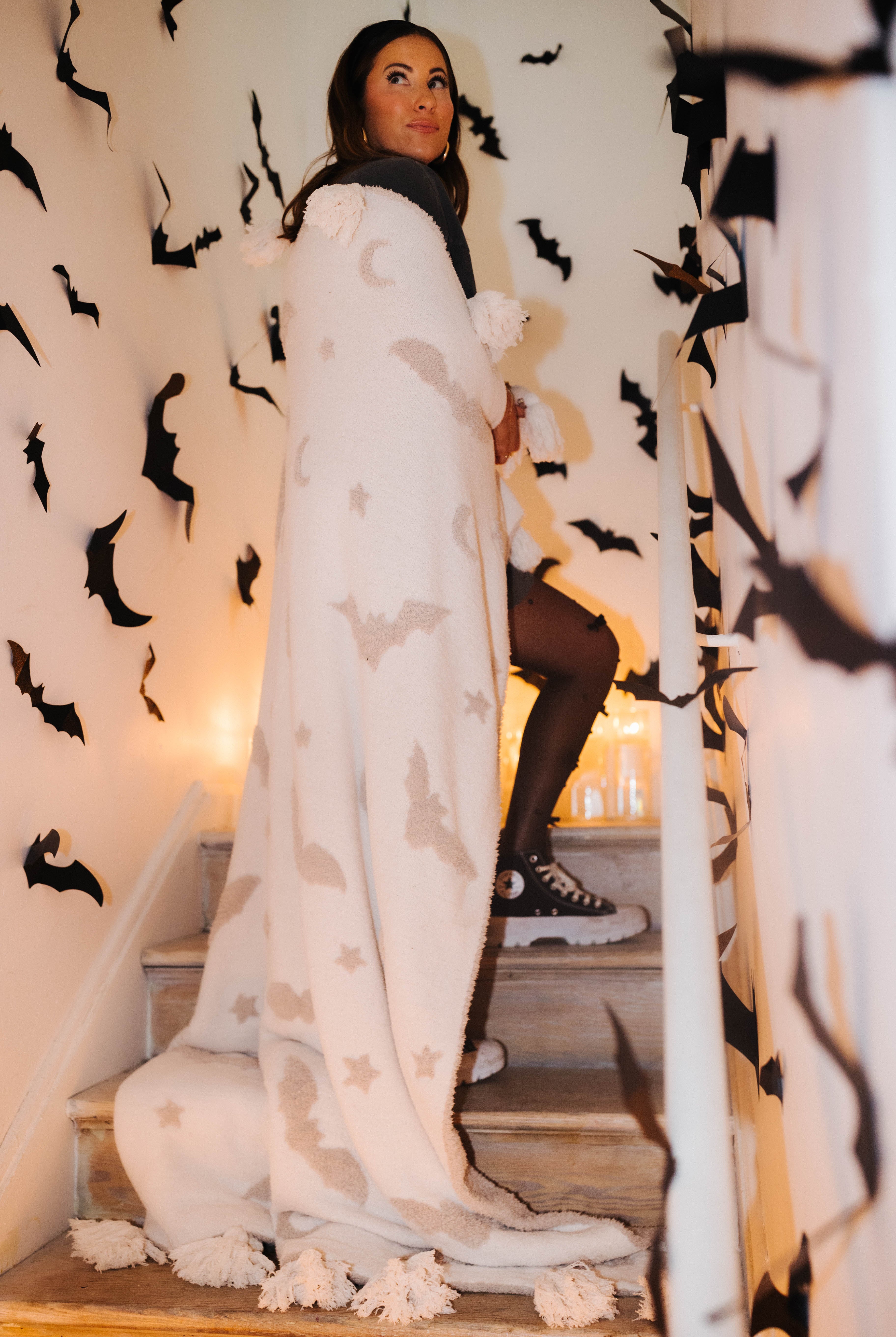 model krista on staircase with bat tassel blanket wrapped around with bat decorations in the background