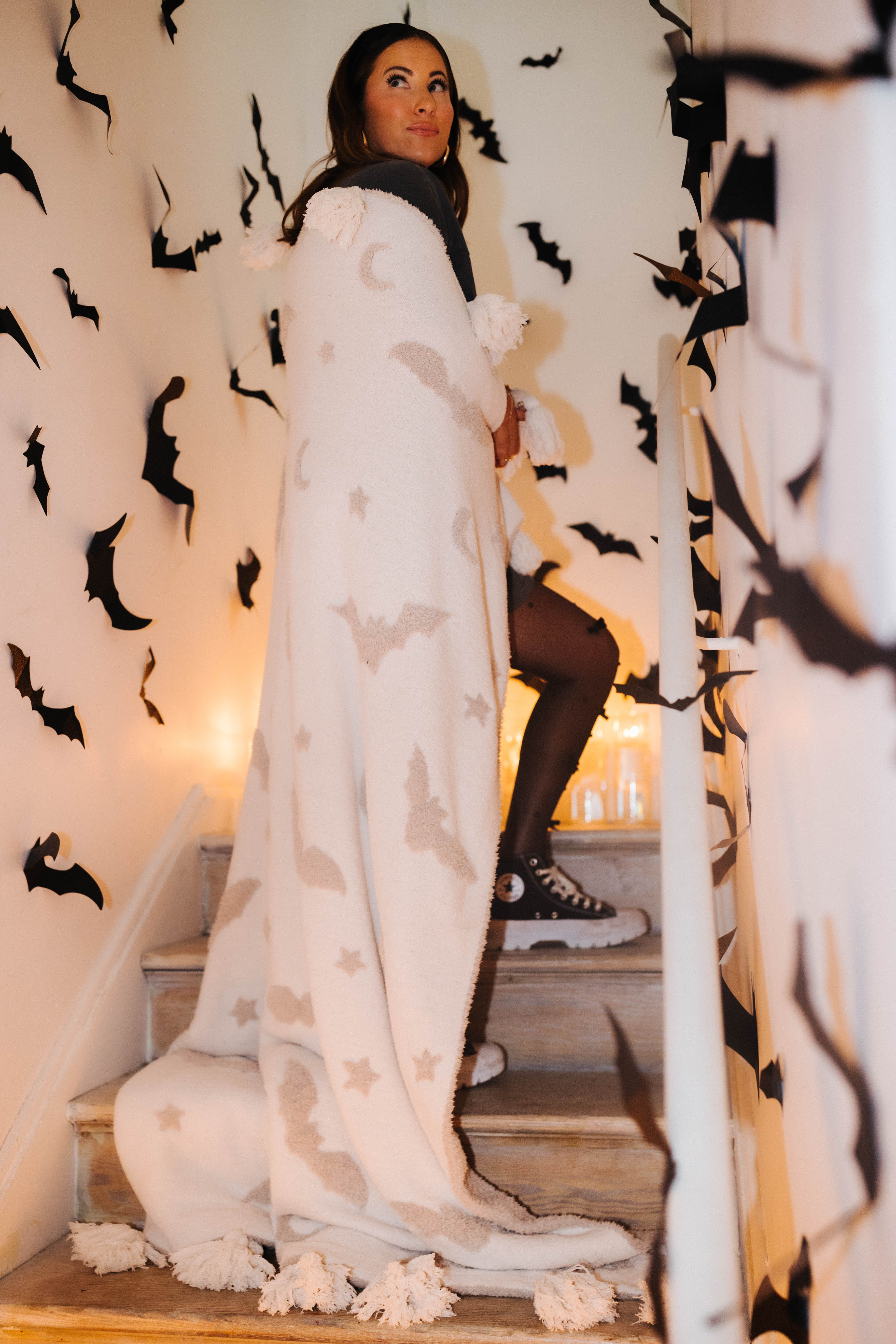 model krista on staircase with bat tassel blanket wrapped around with bat decorations in the background