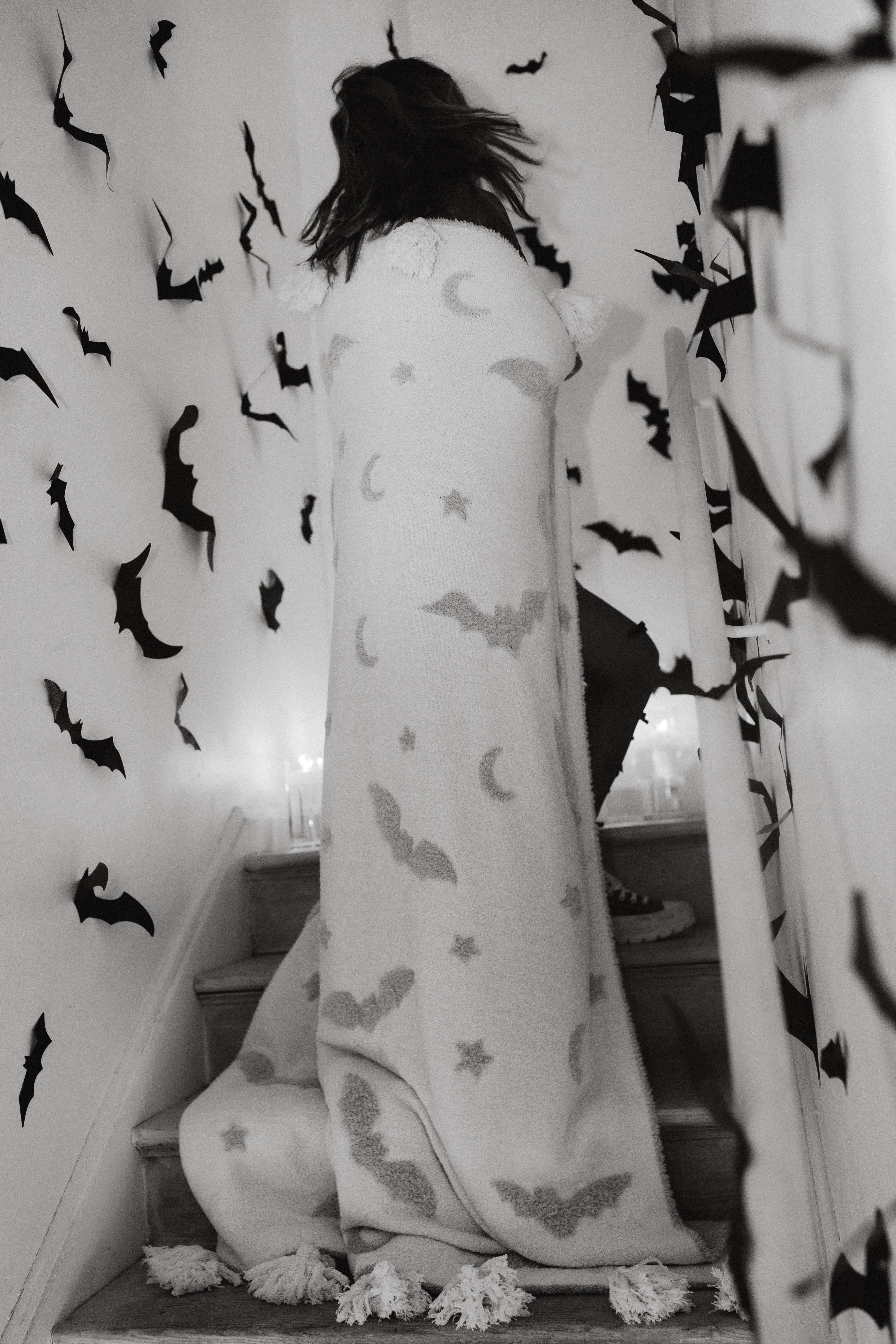 model with bat tassel blanket on staircase with bat decorations in the background it is a black and white photo