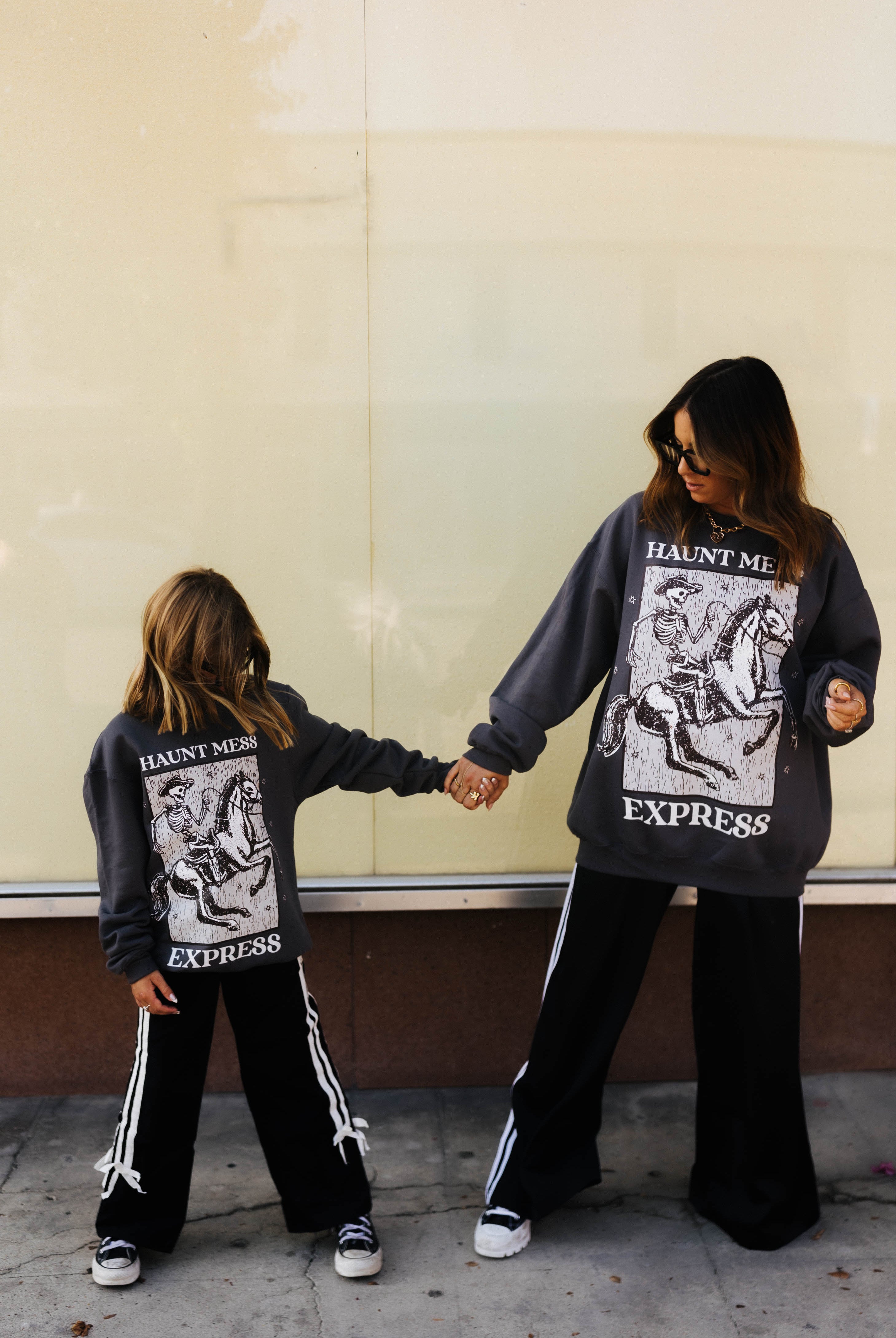 models krista and kolly wearing adult and youth haunt mess express sweatshirts looking down at sweatshirts