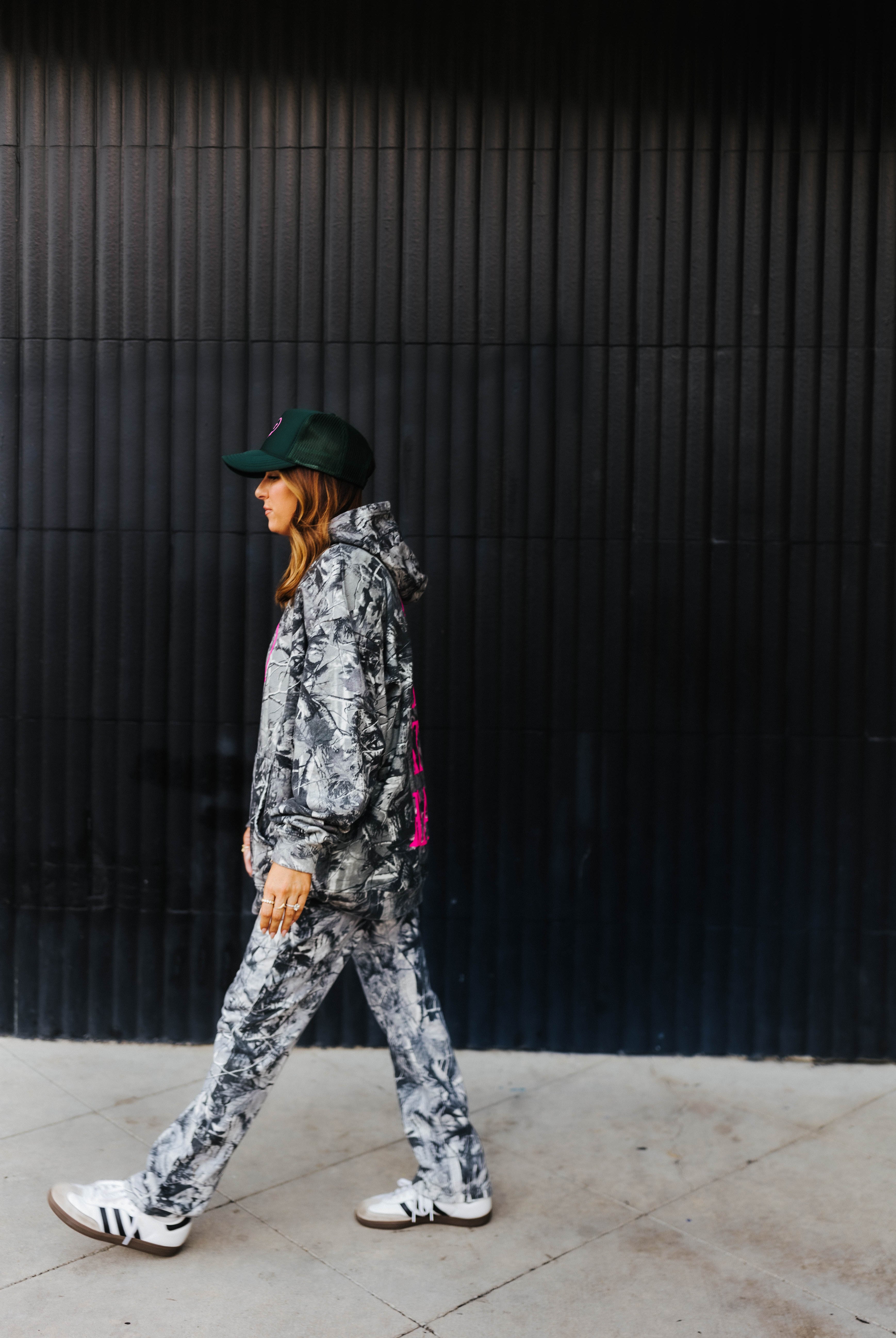 model walking away showing hot mess at heart camo hoodie and hot mess at heart hat against black wall