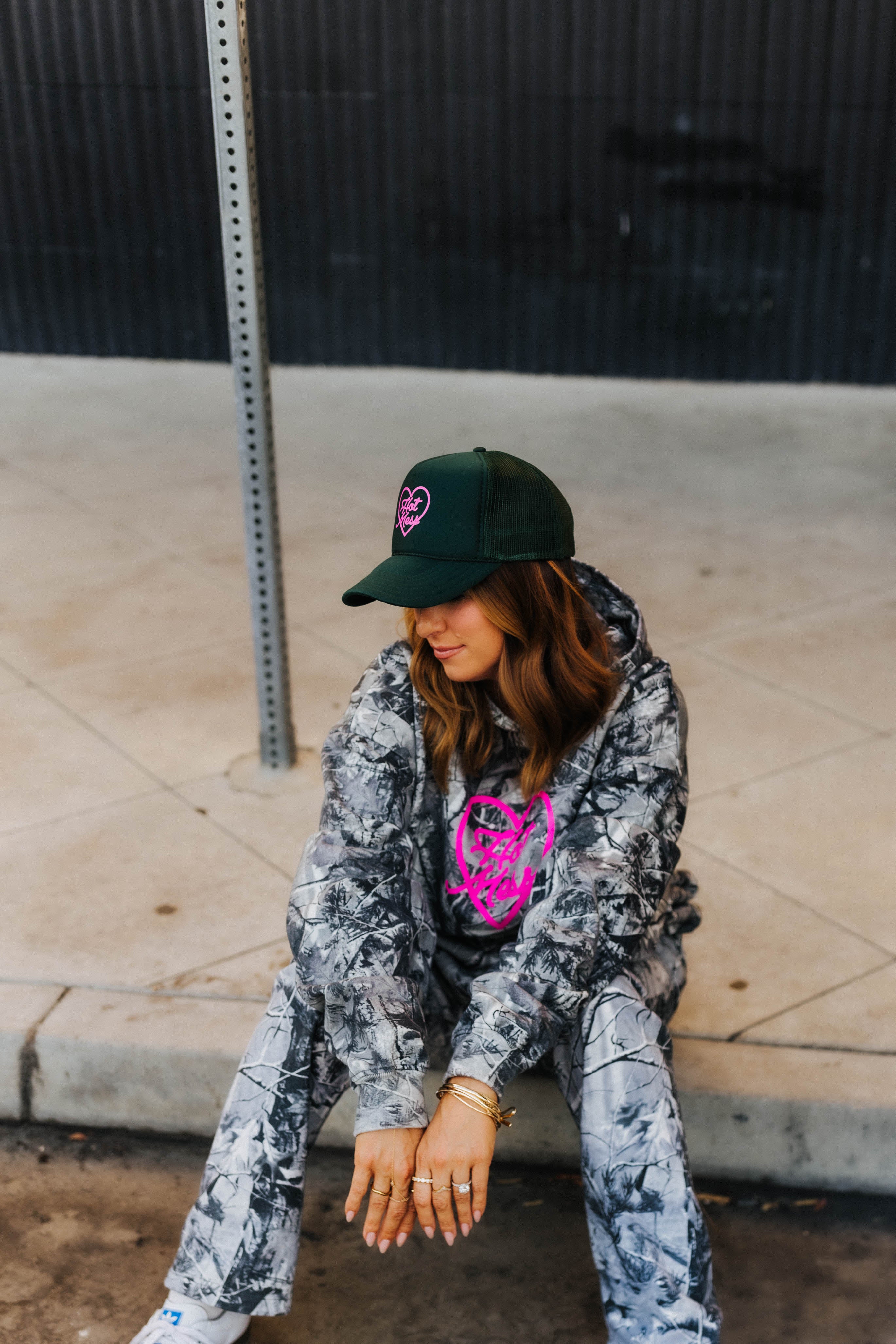 model sitting on curb wearing hot mess at heart camo set and hot mess at heart dark green hat