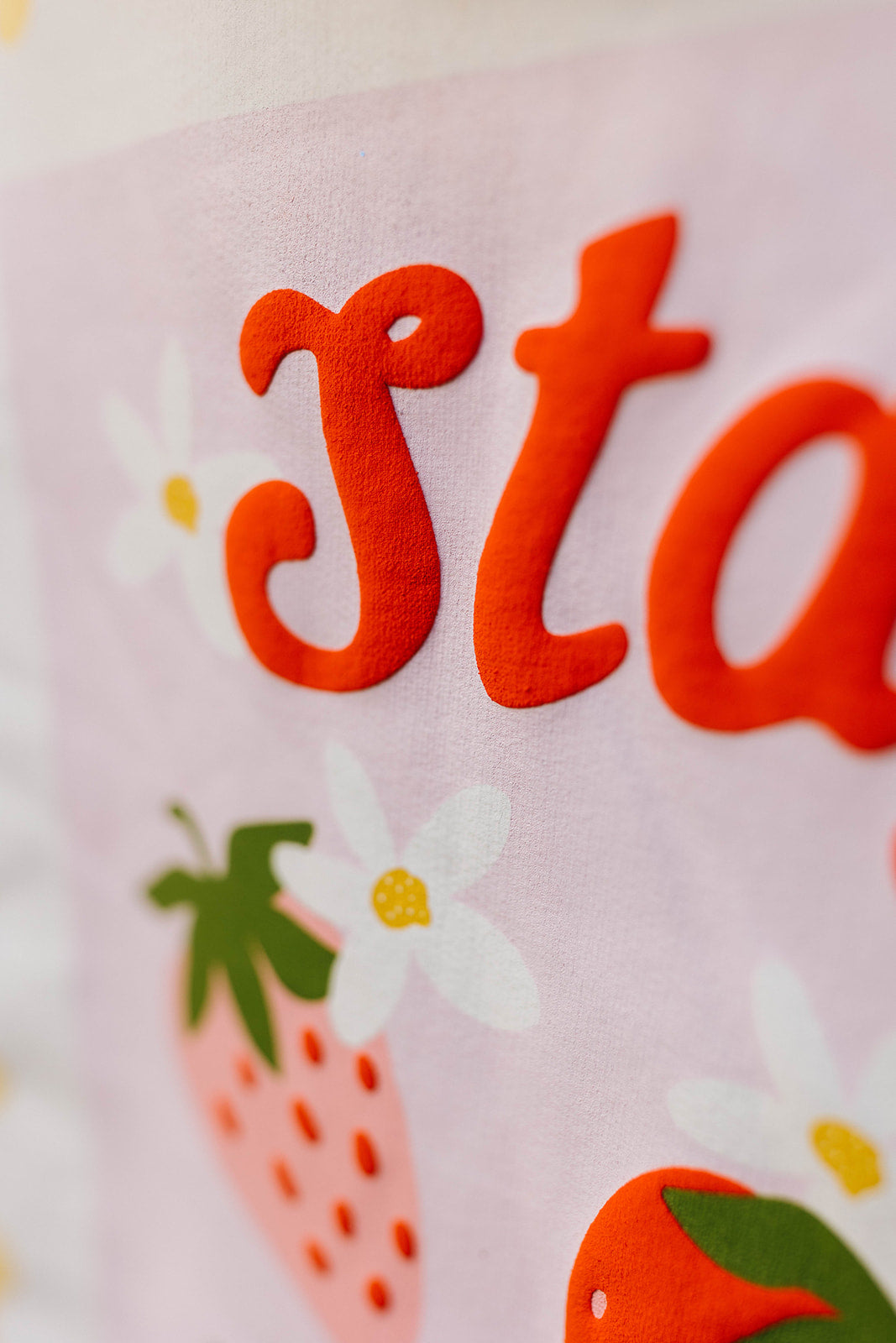 Close-up of a pink fabric with red text, strawberries, and flowers.