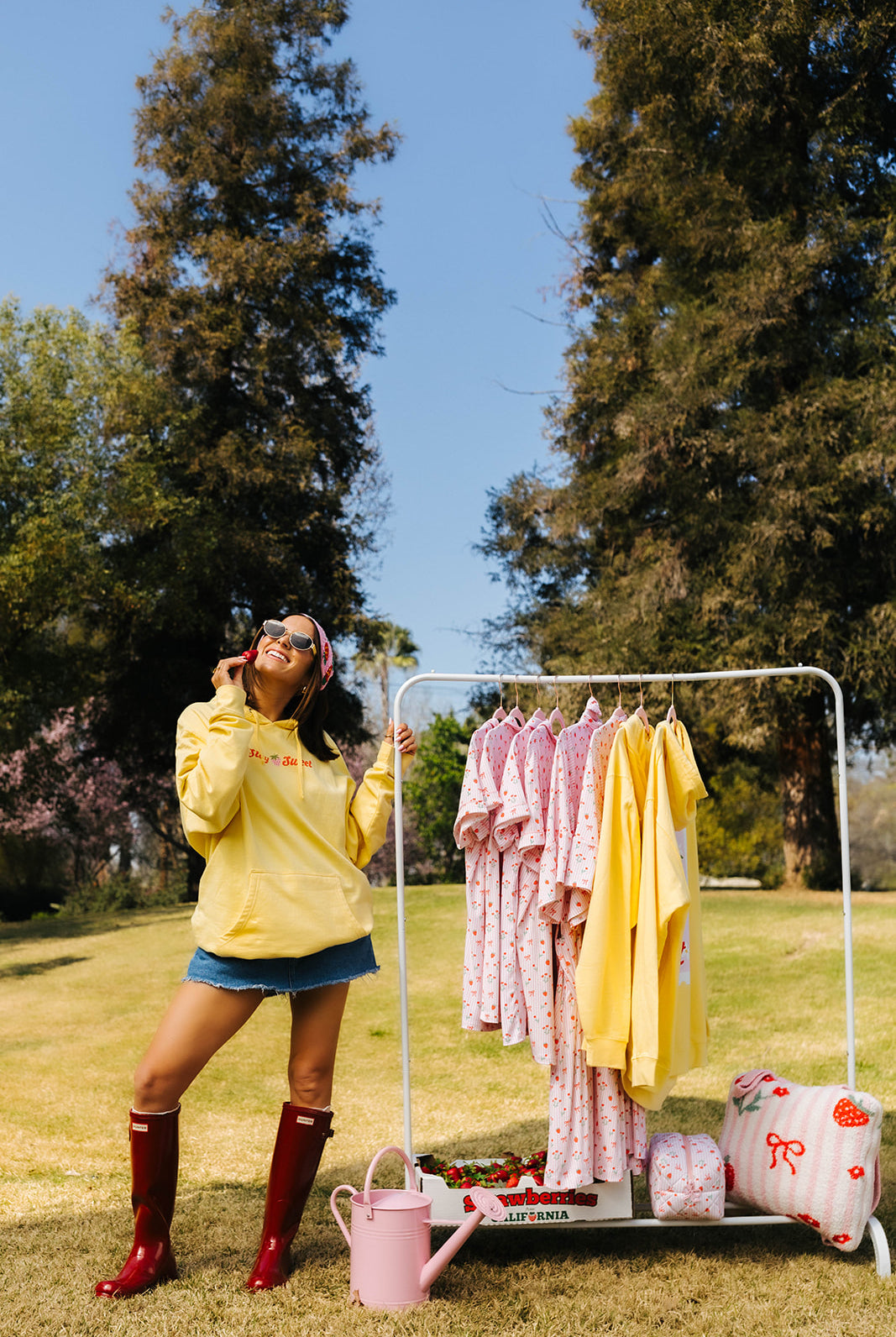 Person in a yellow sweatshirt
standing next to a clothing rack with various outfits outdoors.