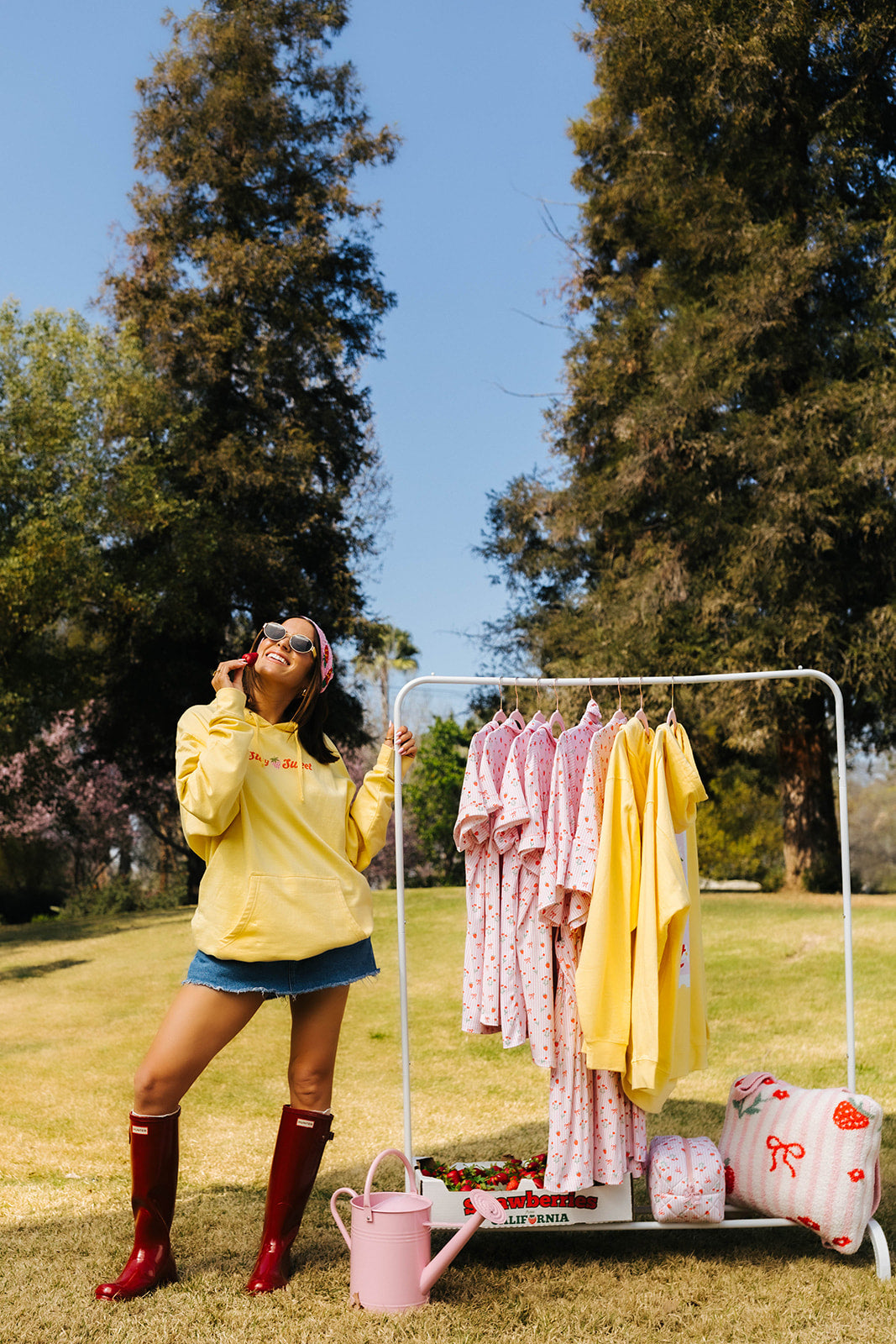 Person in a yellow sweatshirt
standing next to a clothing rack with various outfits outdoors.