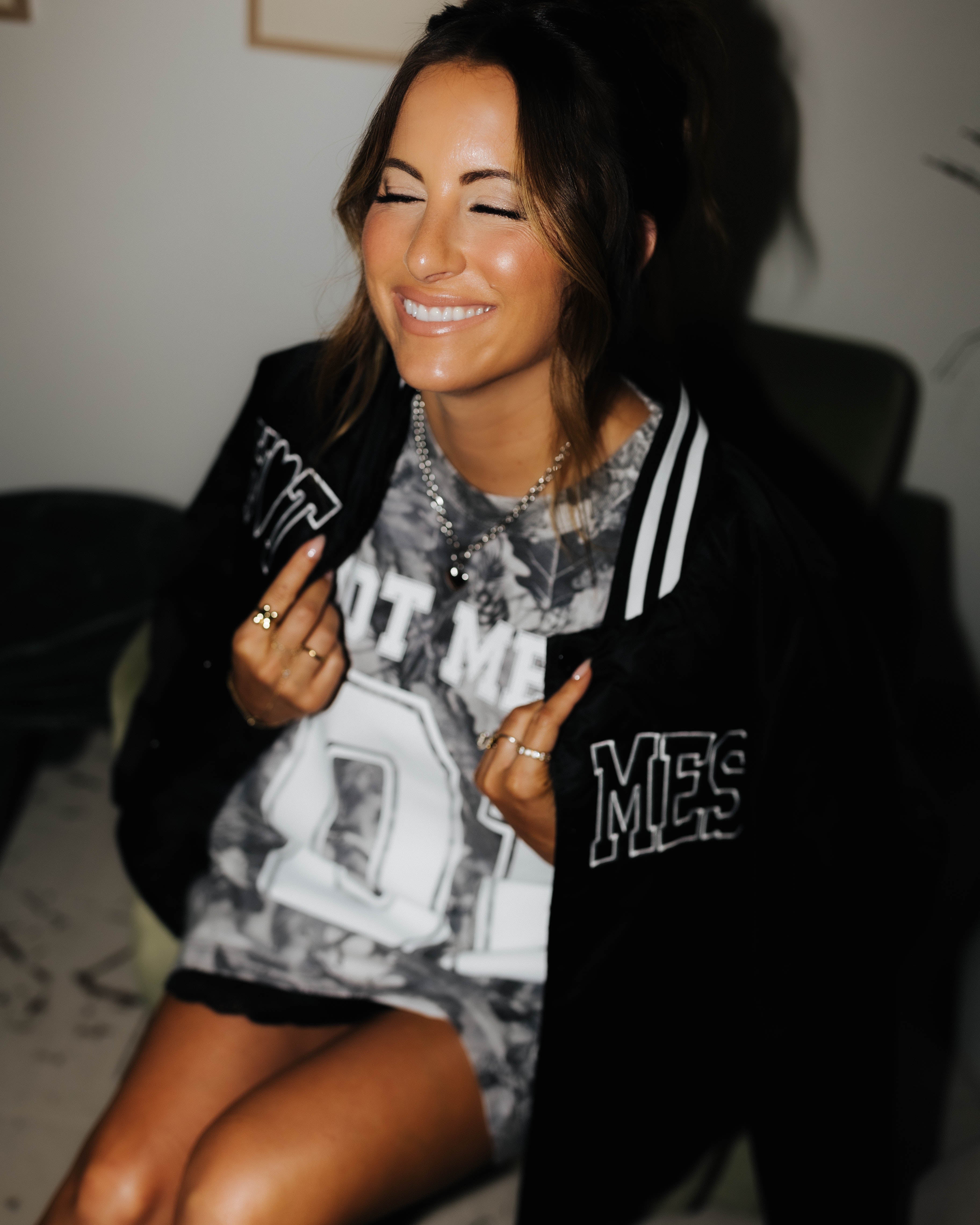 model smiling with eyes closed holding the hot mess bomber jacket over shoulders while wearing camo tee