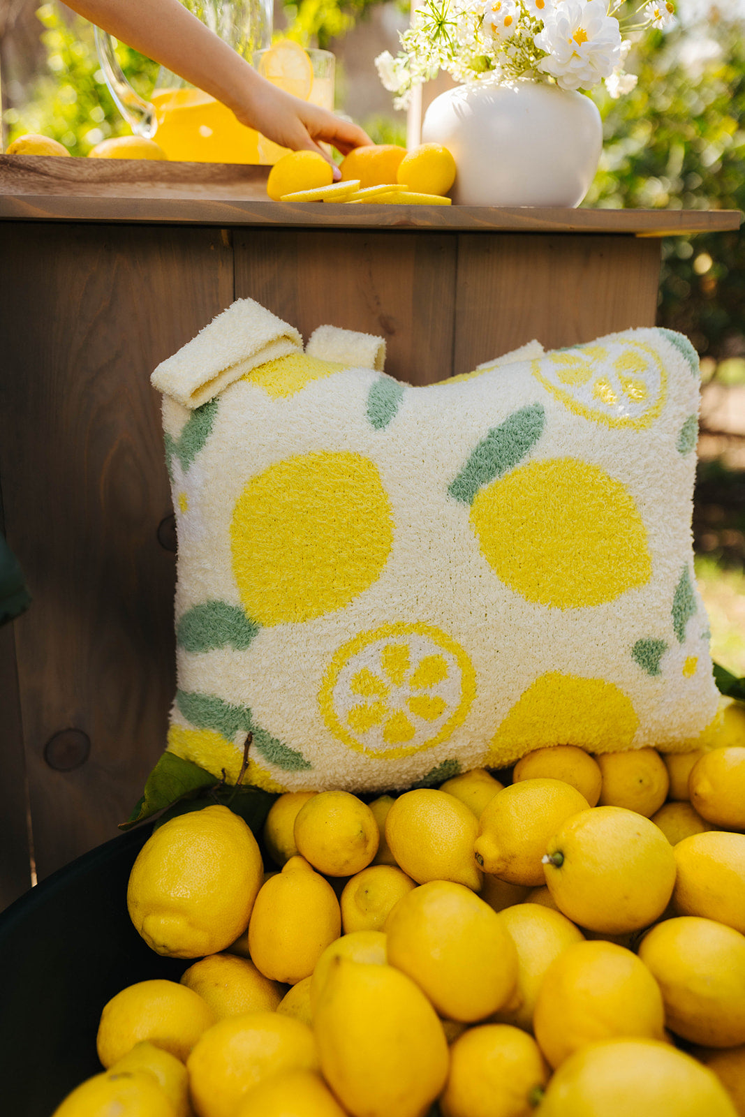 Quillow with lemon pattern surrounded by lemons on a wooden table outdoors.