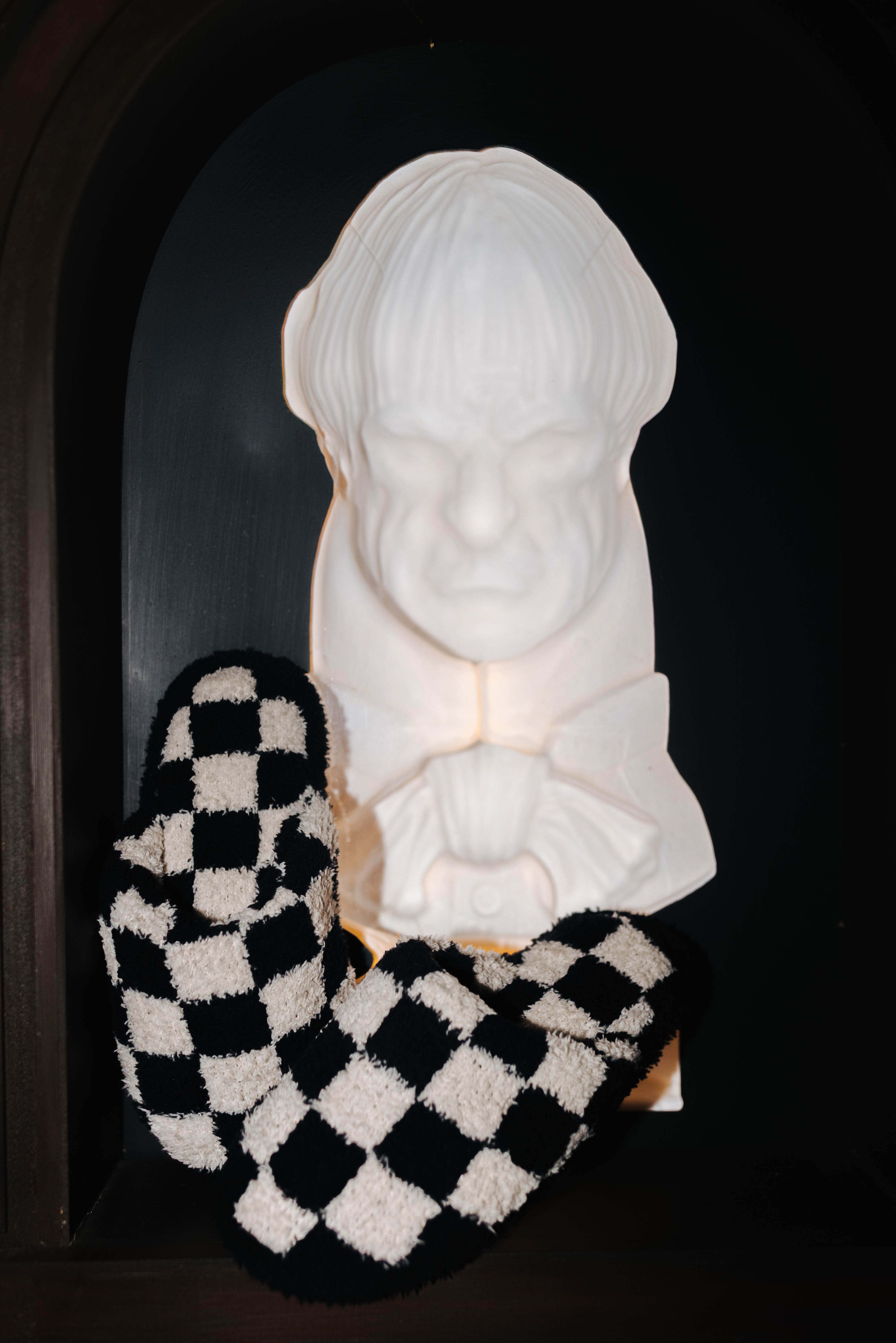 Sand and black check slippers displayed beside a decorative bust
