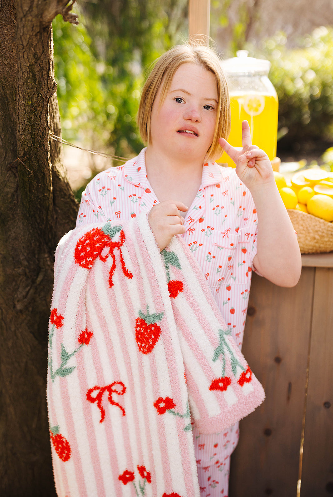 Person wrapped in a pink blanket with red and green patterns, giving a peace sign