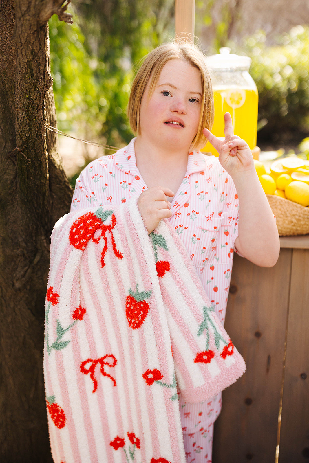 Person wrapped in a pink blanket with red and green patterns, giving a peace sign