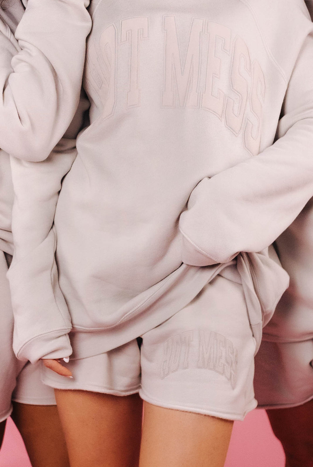 Person wearing a light tan oversized sweater and shorts set on a pink background