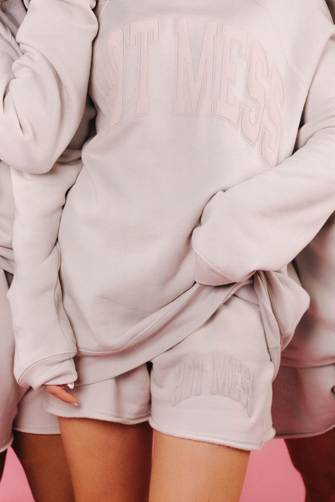 Person wearing a light tan oversized sweater and shorts set on a pink background