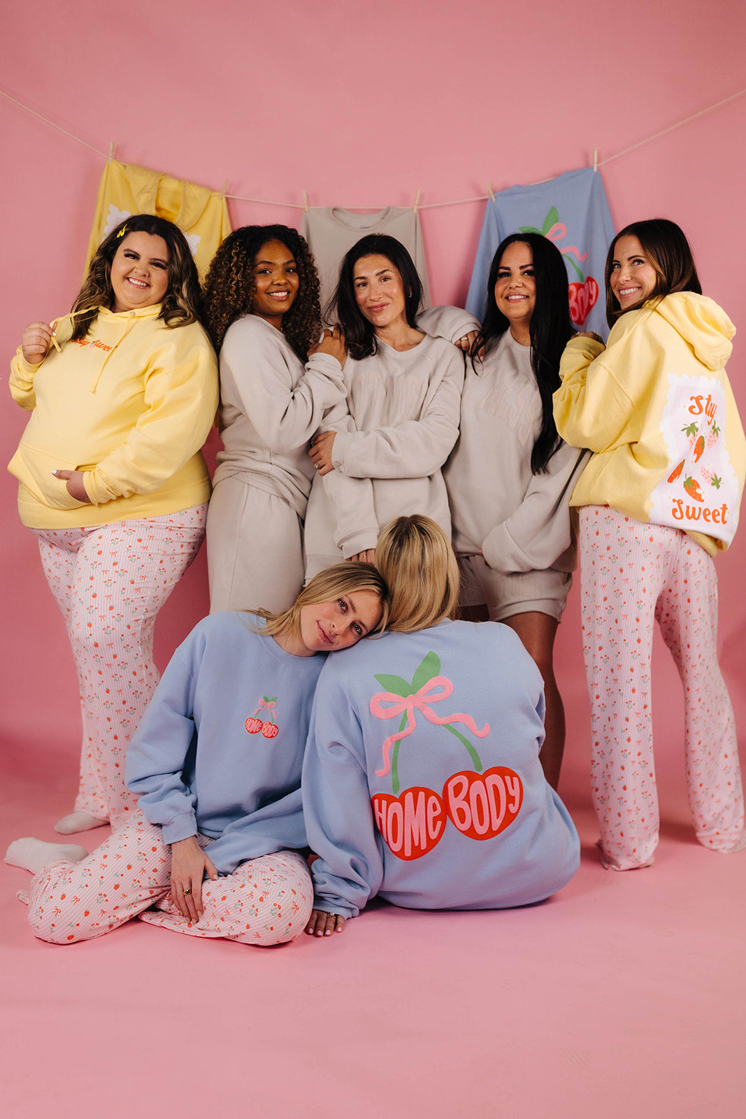 Group of women wearing pajamas and apparel against a pink background