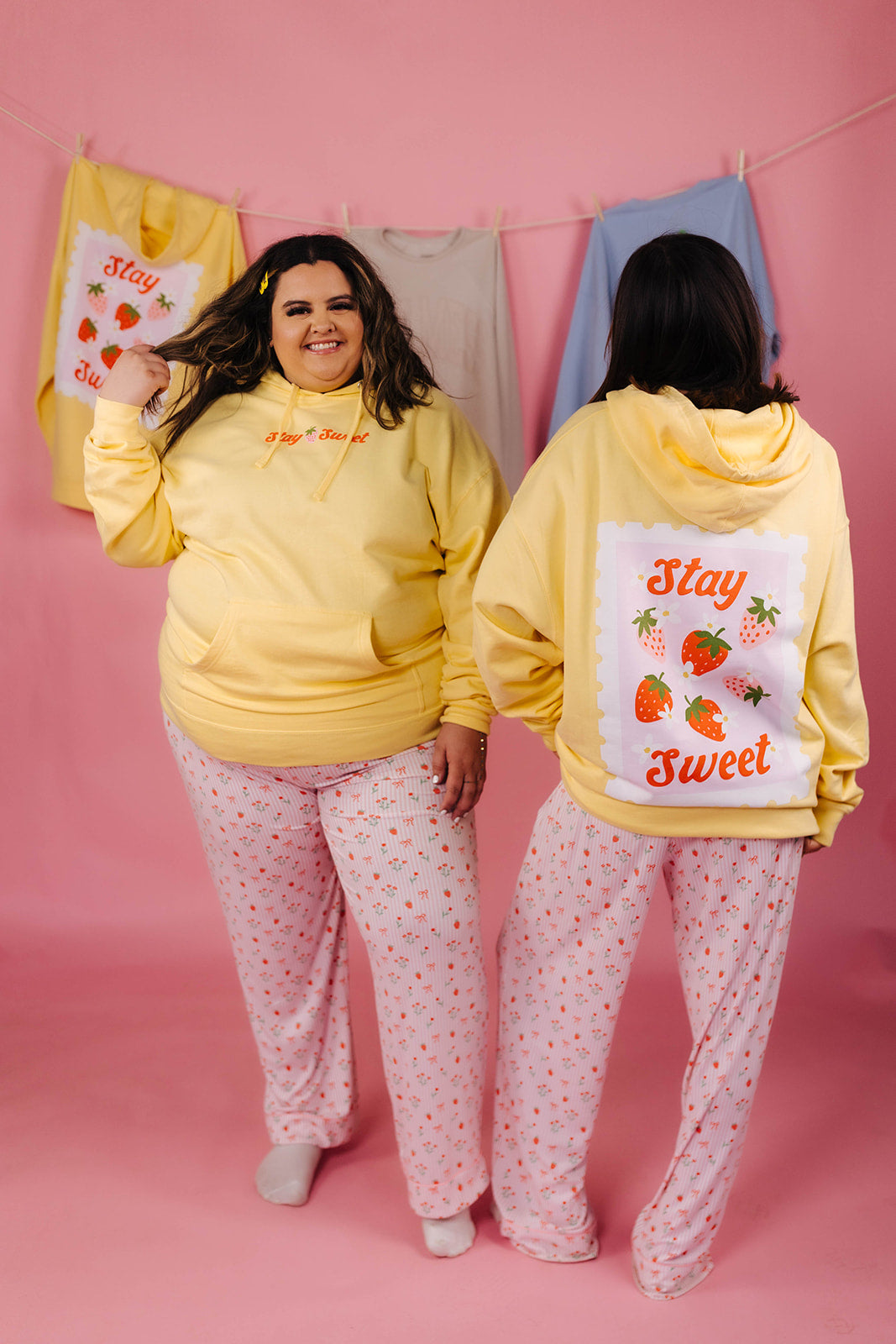 Two people wearing yellow hoodies with a 'Stay Sweet' design on a pink background