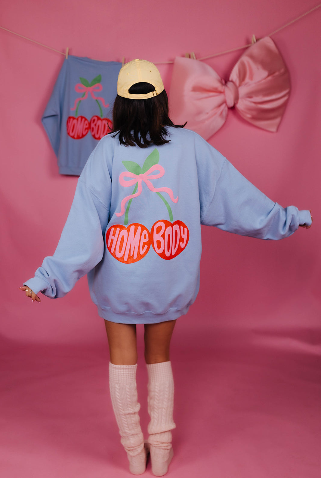 Person wearing a light blue sweatshirt with 'HOME BODY' text on a pink background