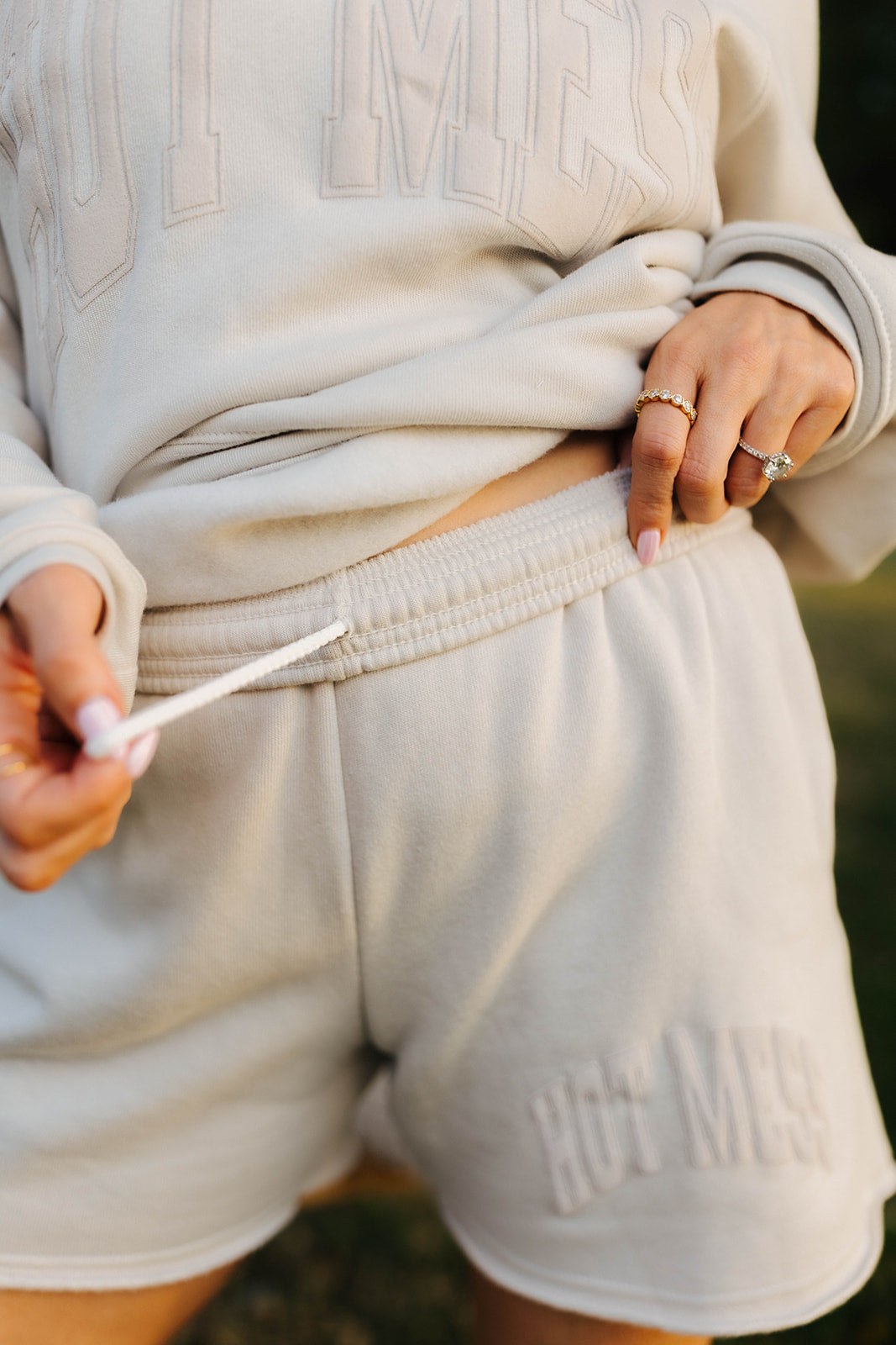 Person wearing a beige track shorts with 'Hot Mess' branding, holding string.