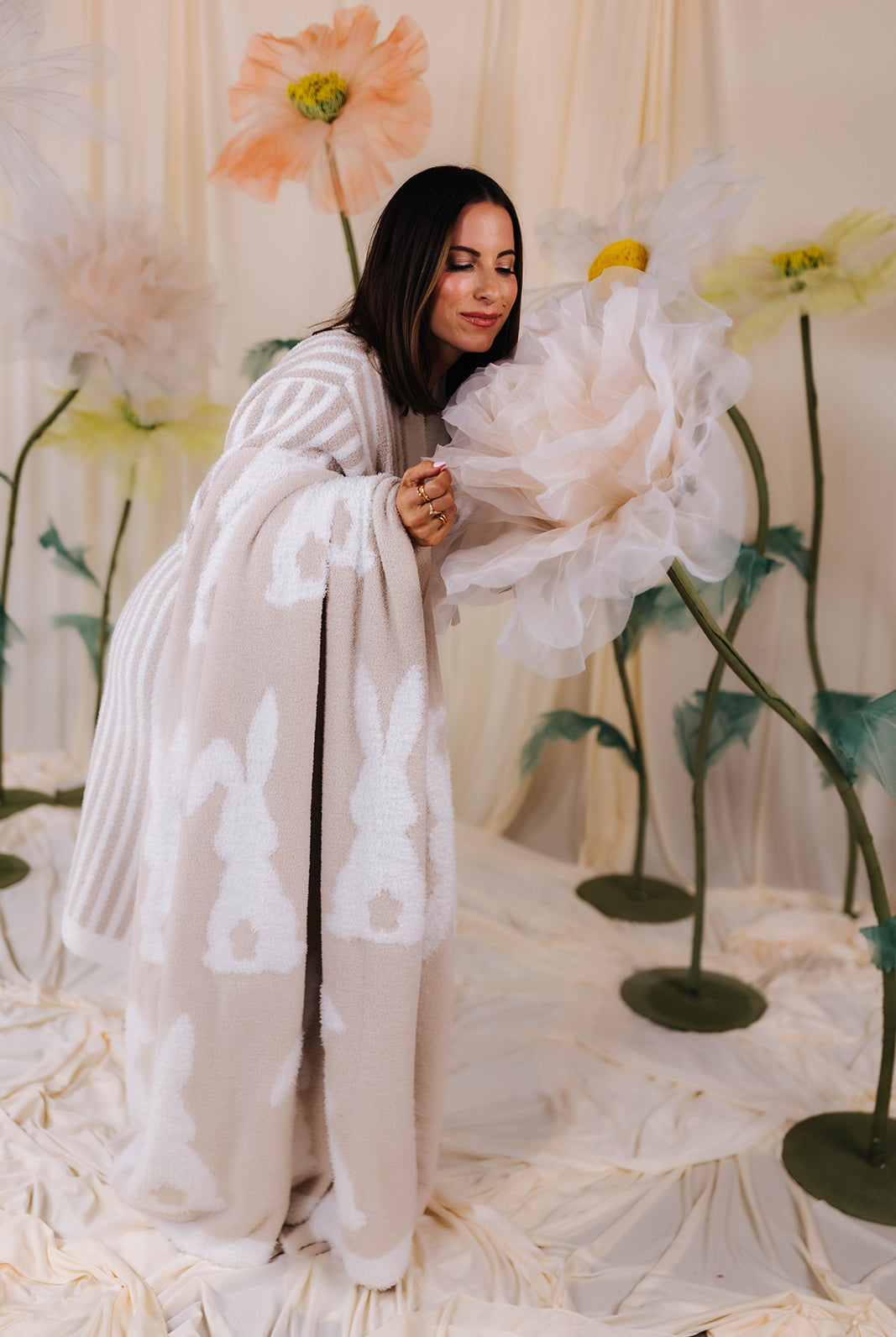 Woman in a robe dress holding a large white flower against a floral backdrop