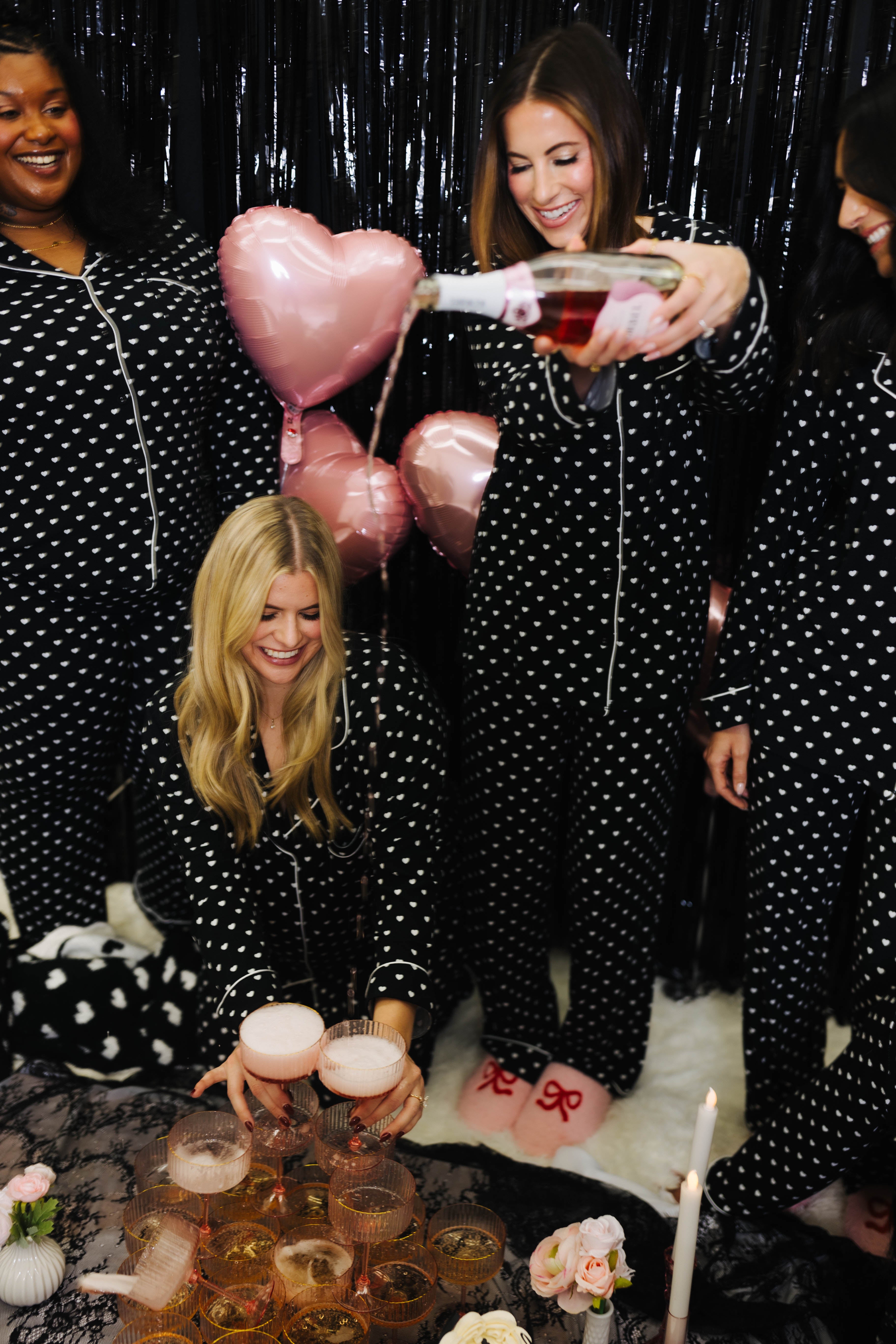 Group of women in polka dot pajamas celebrating with balloons and drinks.