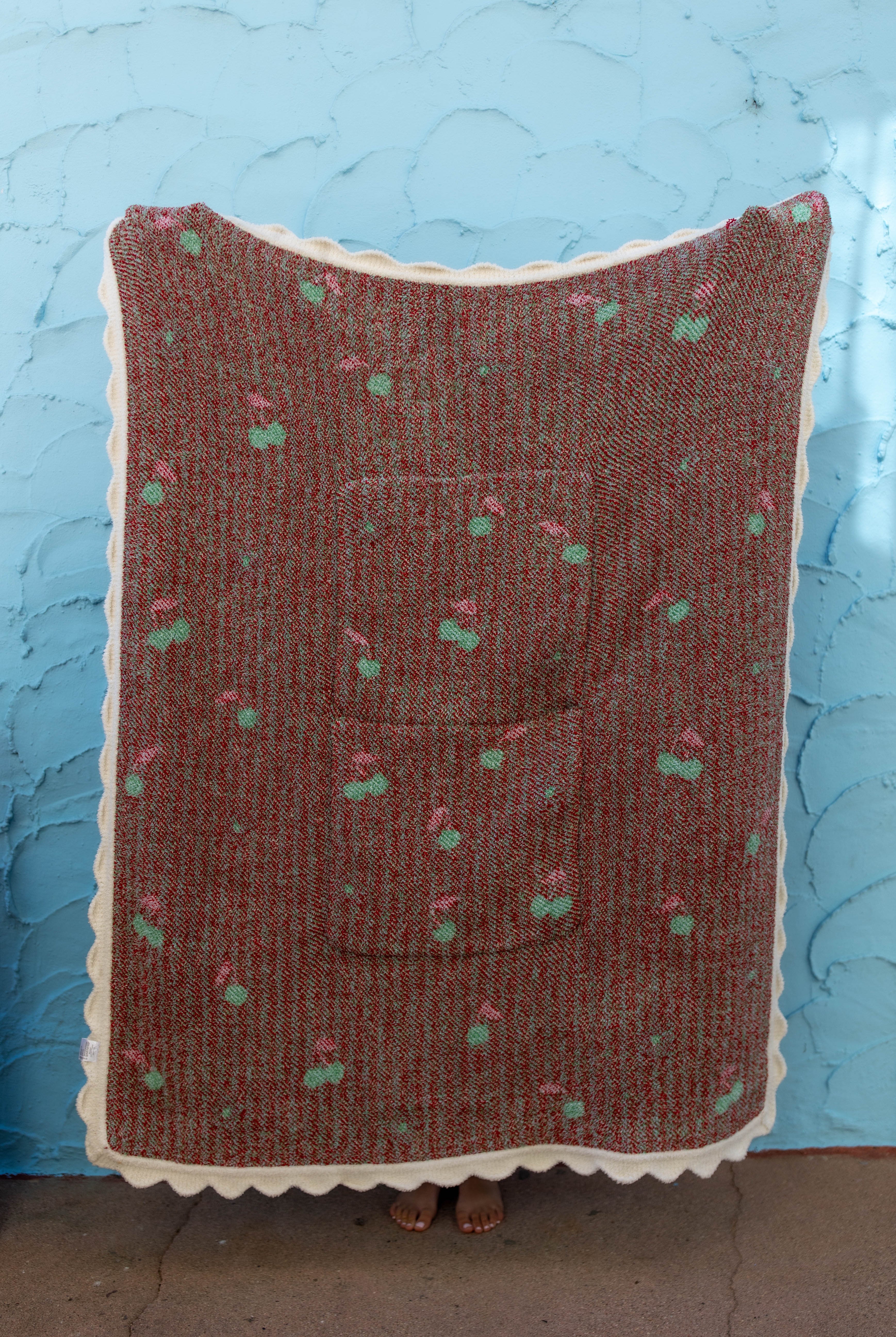 Back side of the cherry blanket showing the white scallop edge and mostly red background against a blue wall