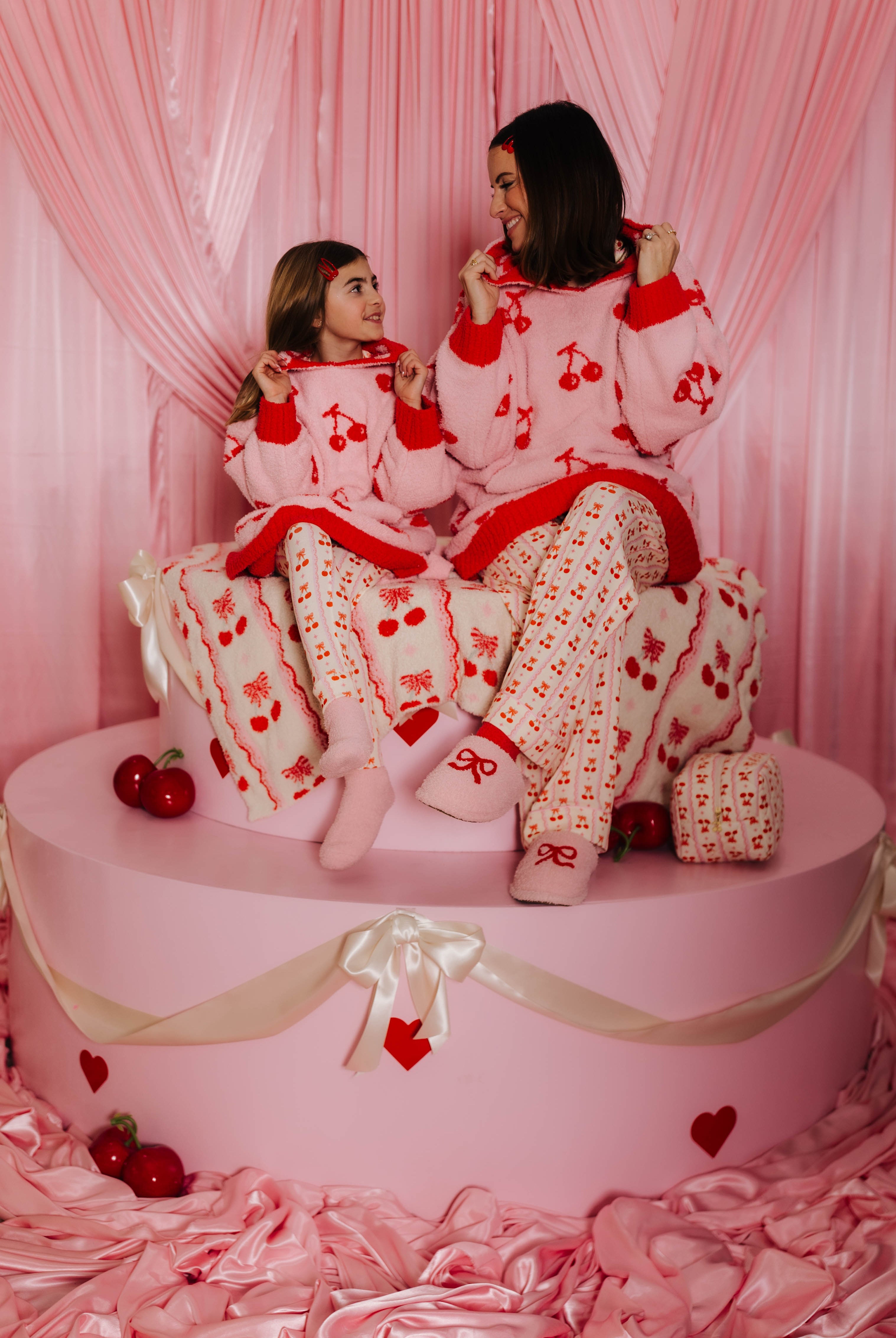 Mother and daughter in matching wearable on a pink cake-shaped platform with heart decorations.