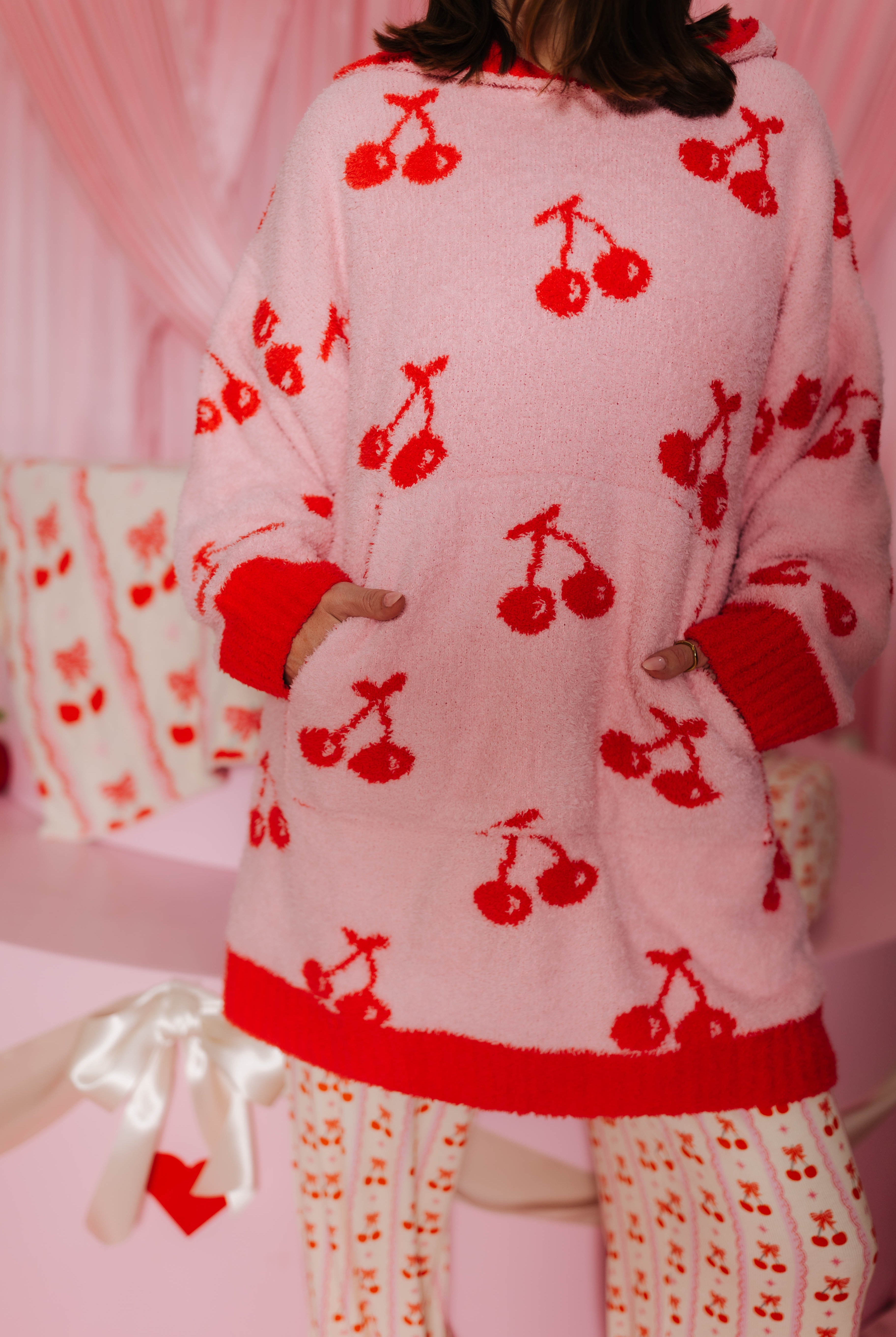 Person wearing a pink wearable with red cherry patterns in a pink room. Showing the pockets.