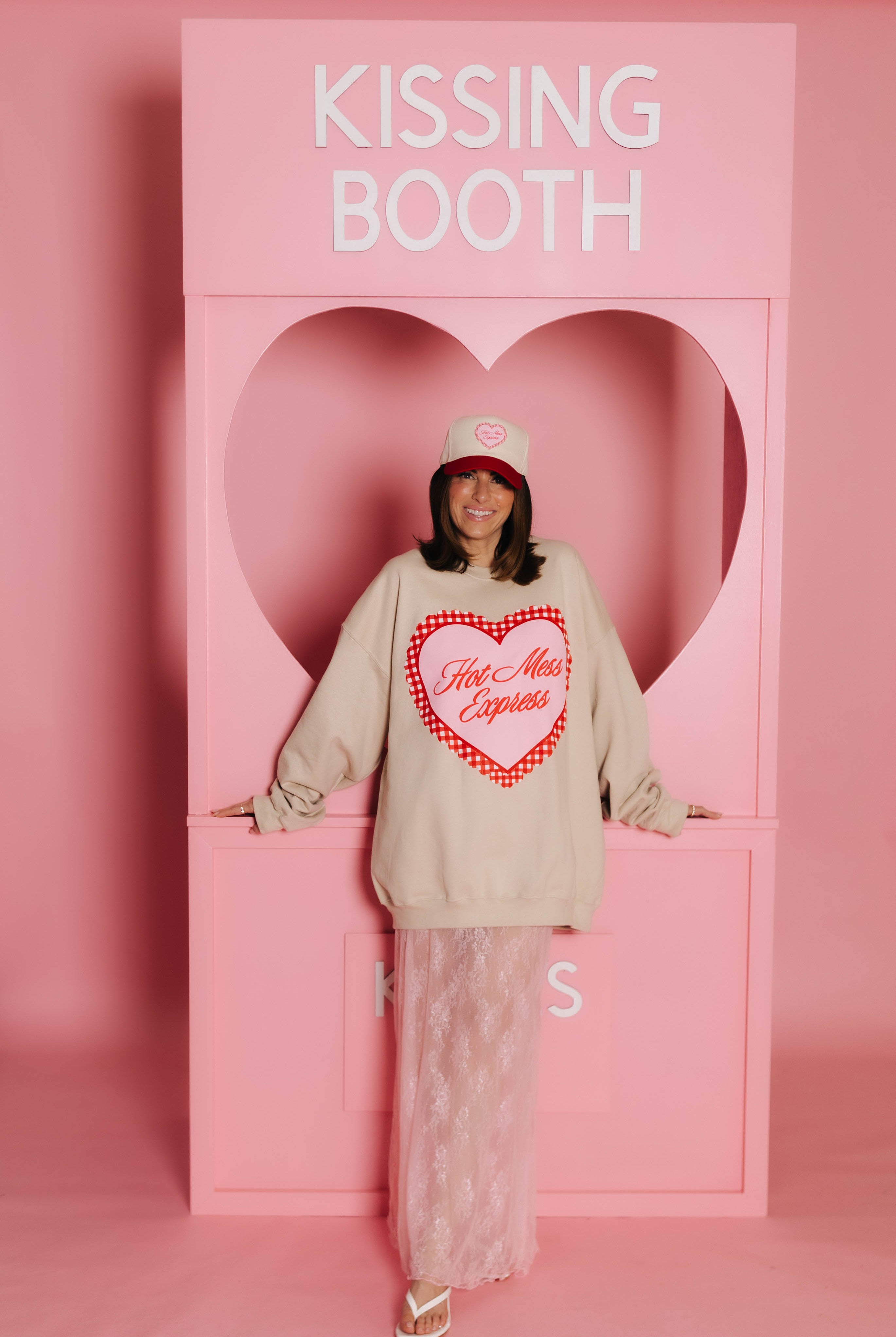 Krista standing in front of the kissing booth modeling the hot mess express sweatshirt.