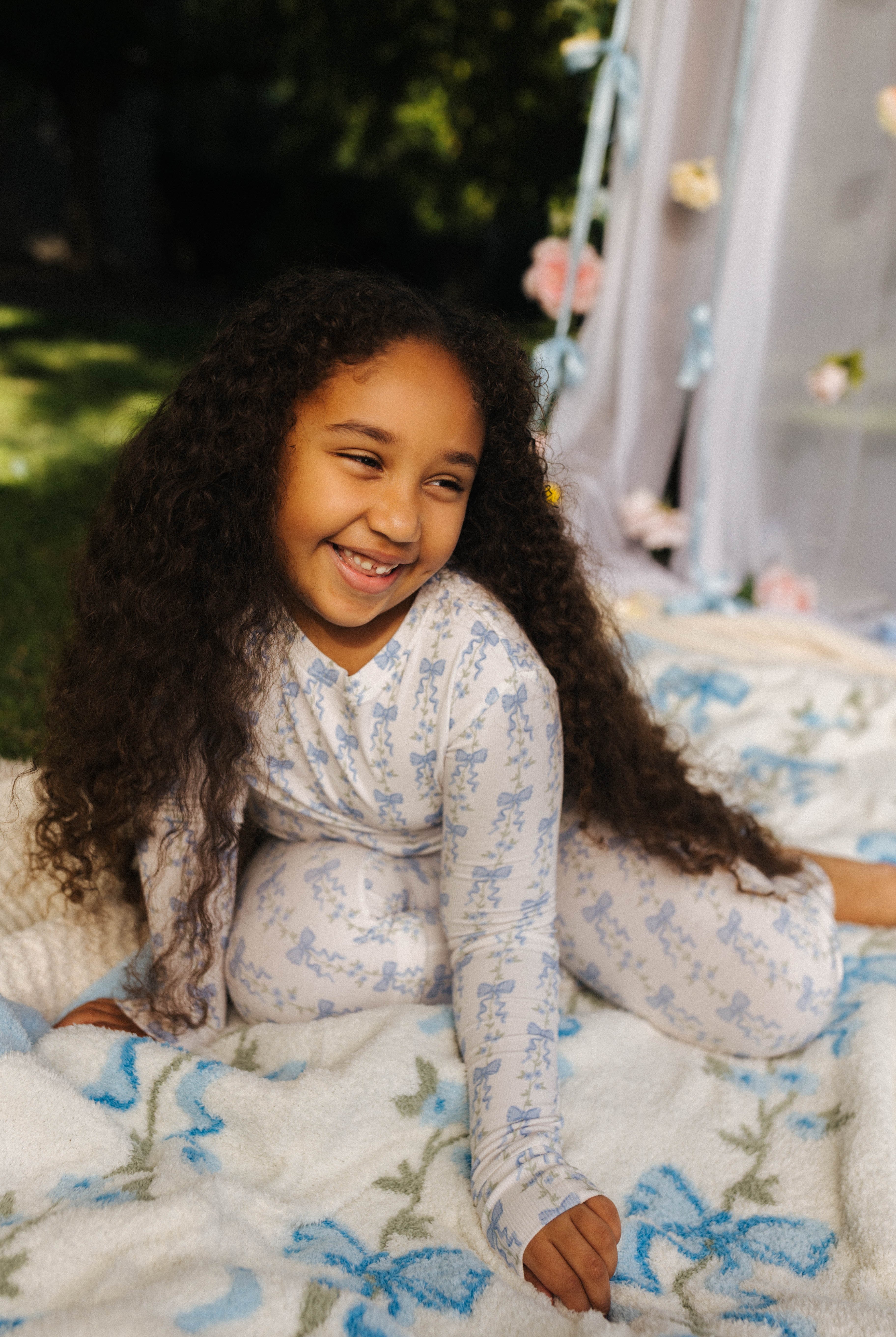 Child posing and smiling on the blow bow blanket in the blue bow pjs