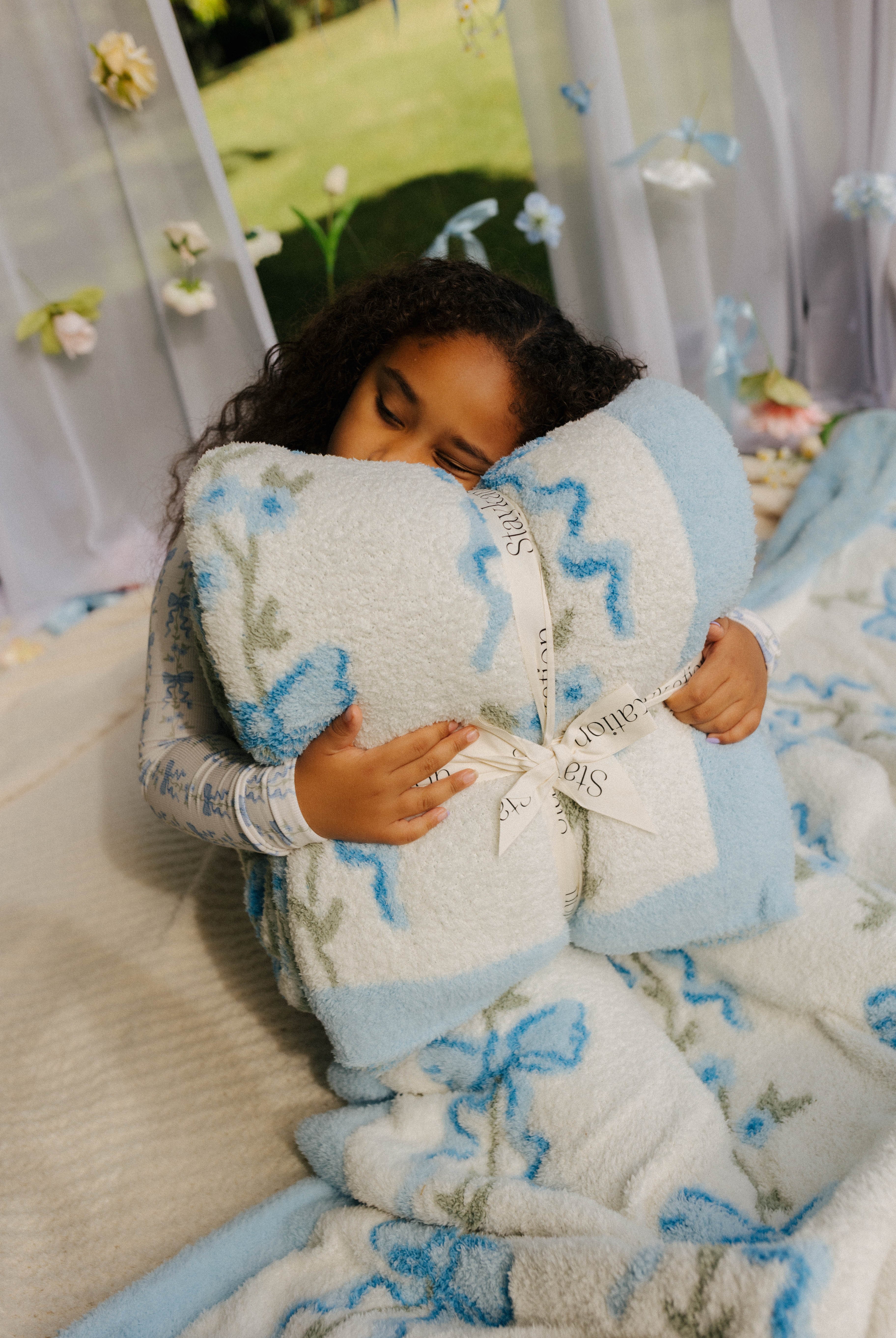 Child holding a blue and white patterned blanket with the bow label