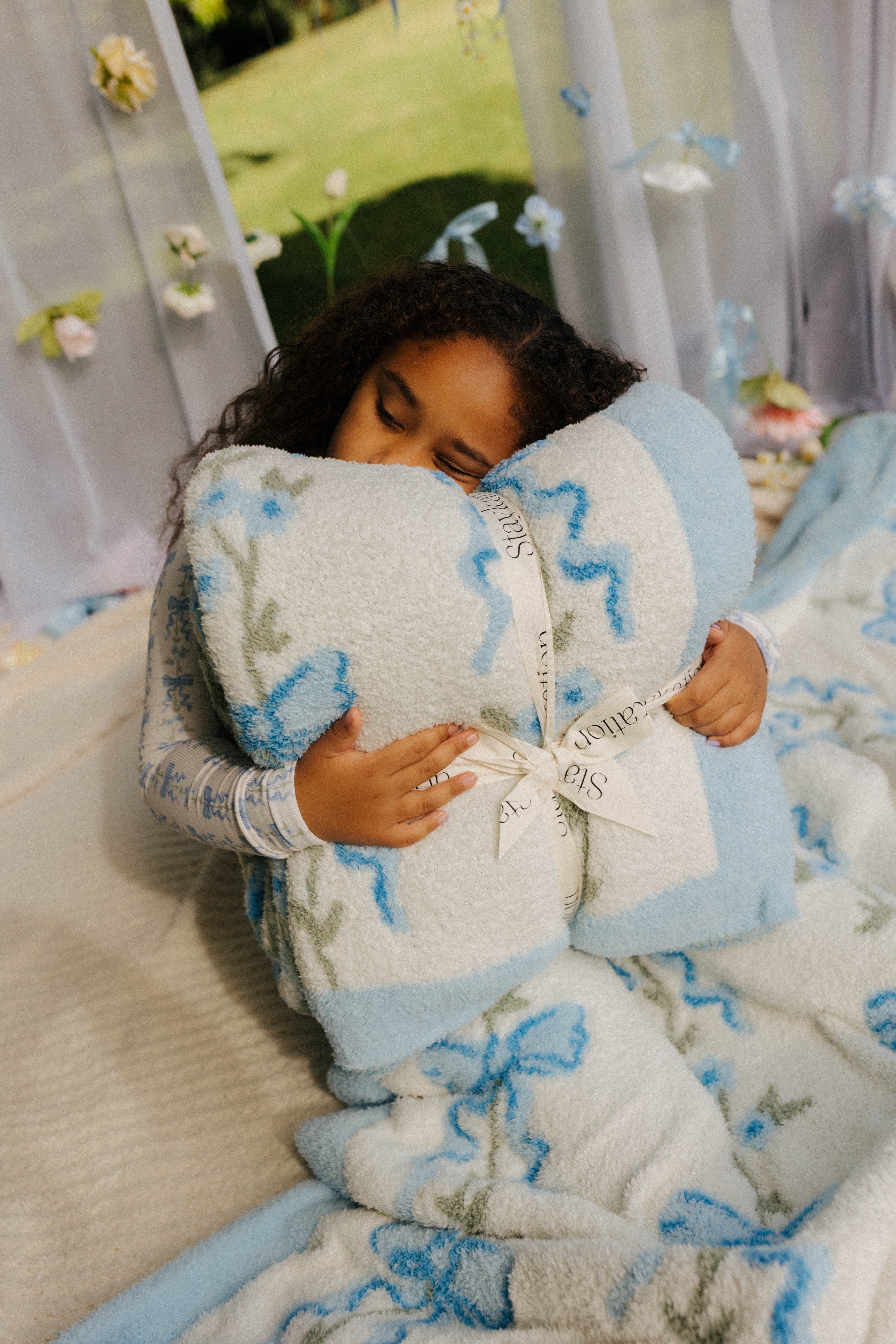 Child holding a blue and white patterned blanket with the bow label