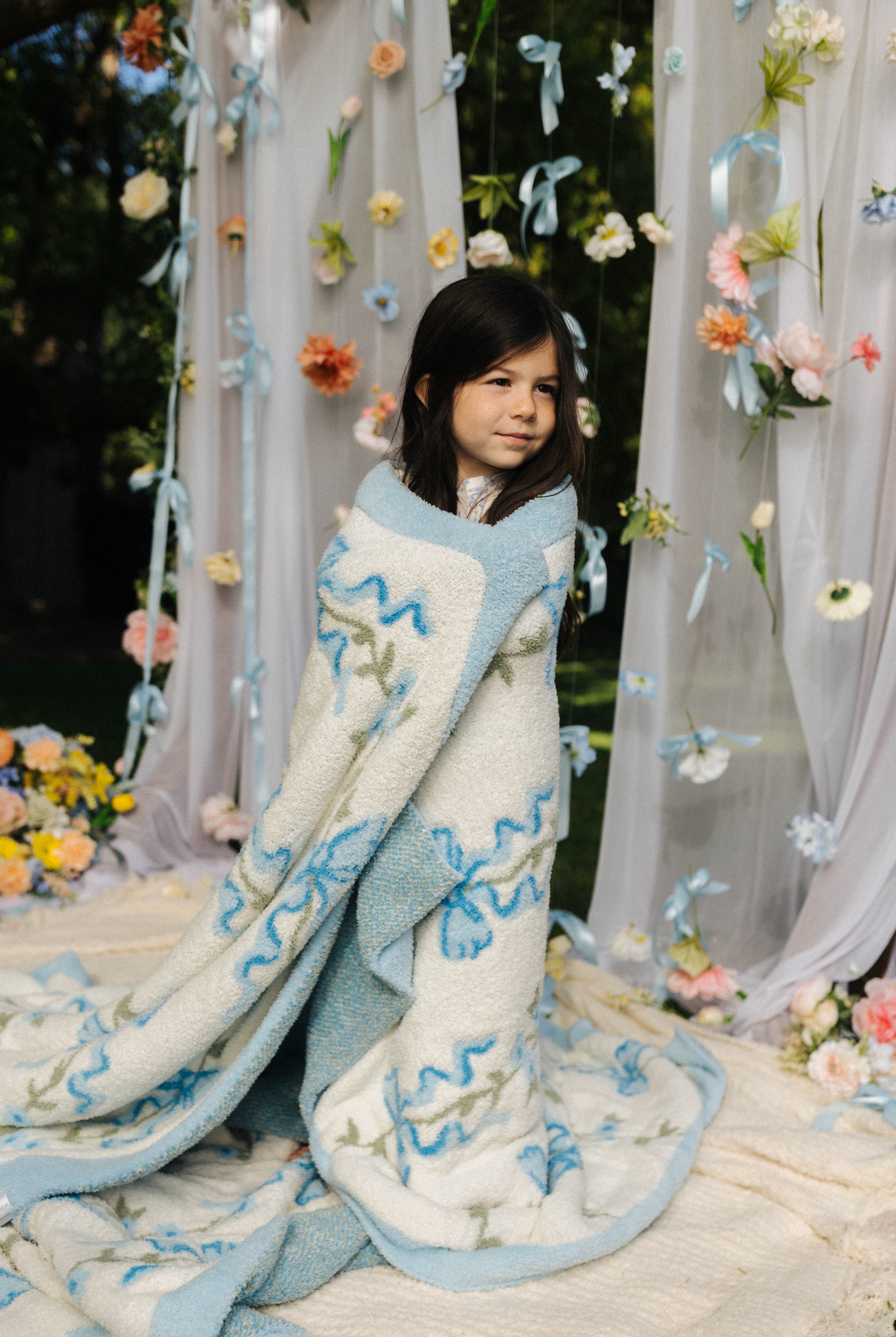 Child wrapped in a blue and white patterned blanket with floral and decorative background