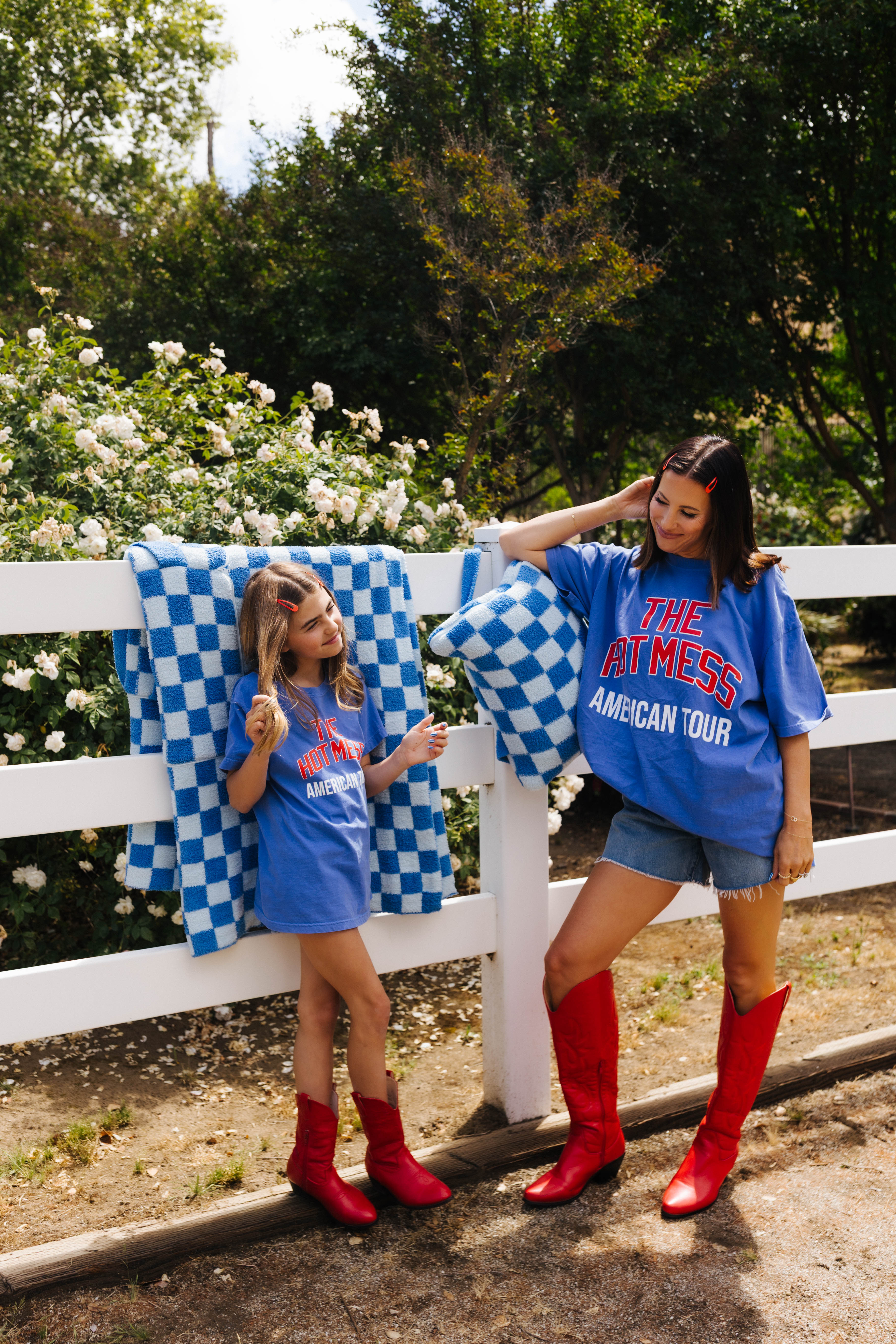 Two girls in blue shirts and red boots standing next to a white fence