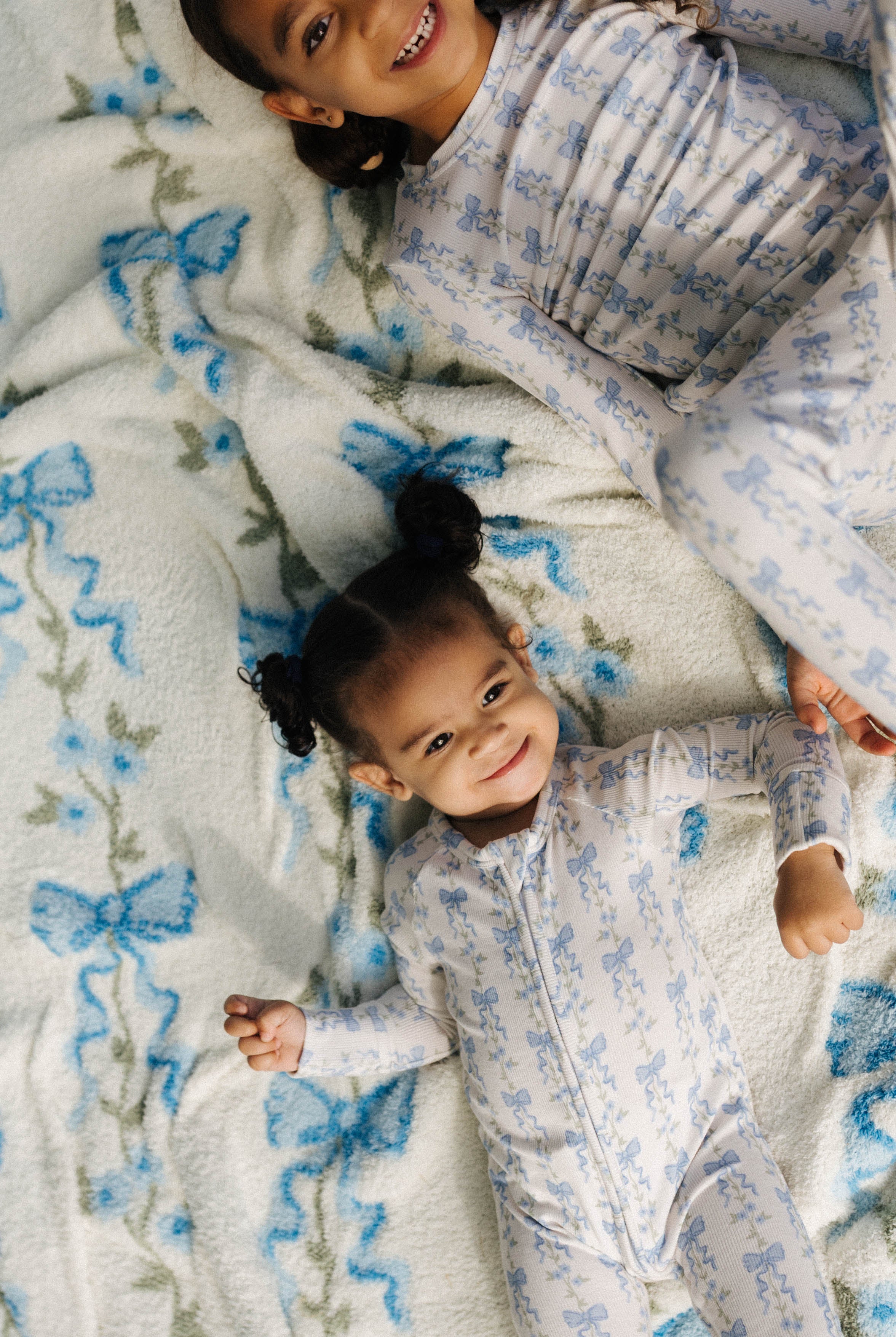 Two children in matching floral pajamas lying on a white blanket with blue floral patterns.