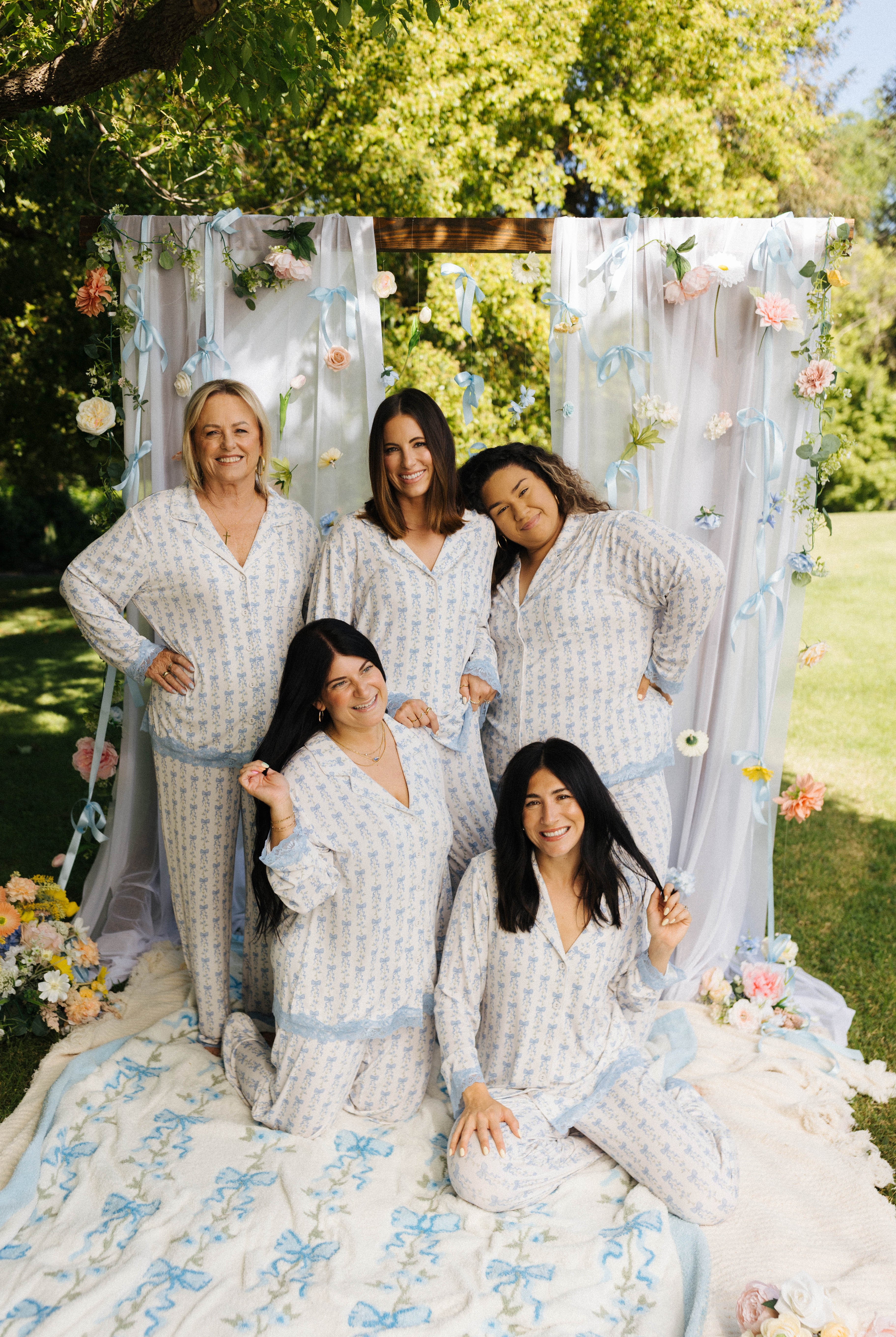All models posing in blue bow floral pjs with greenery and floral sin the background
