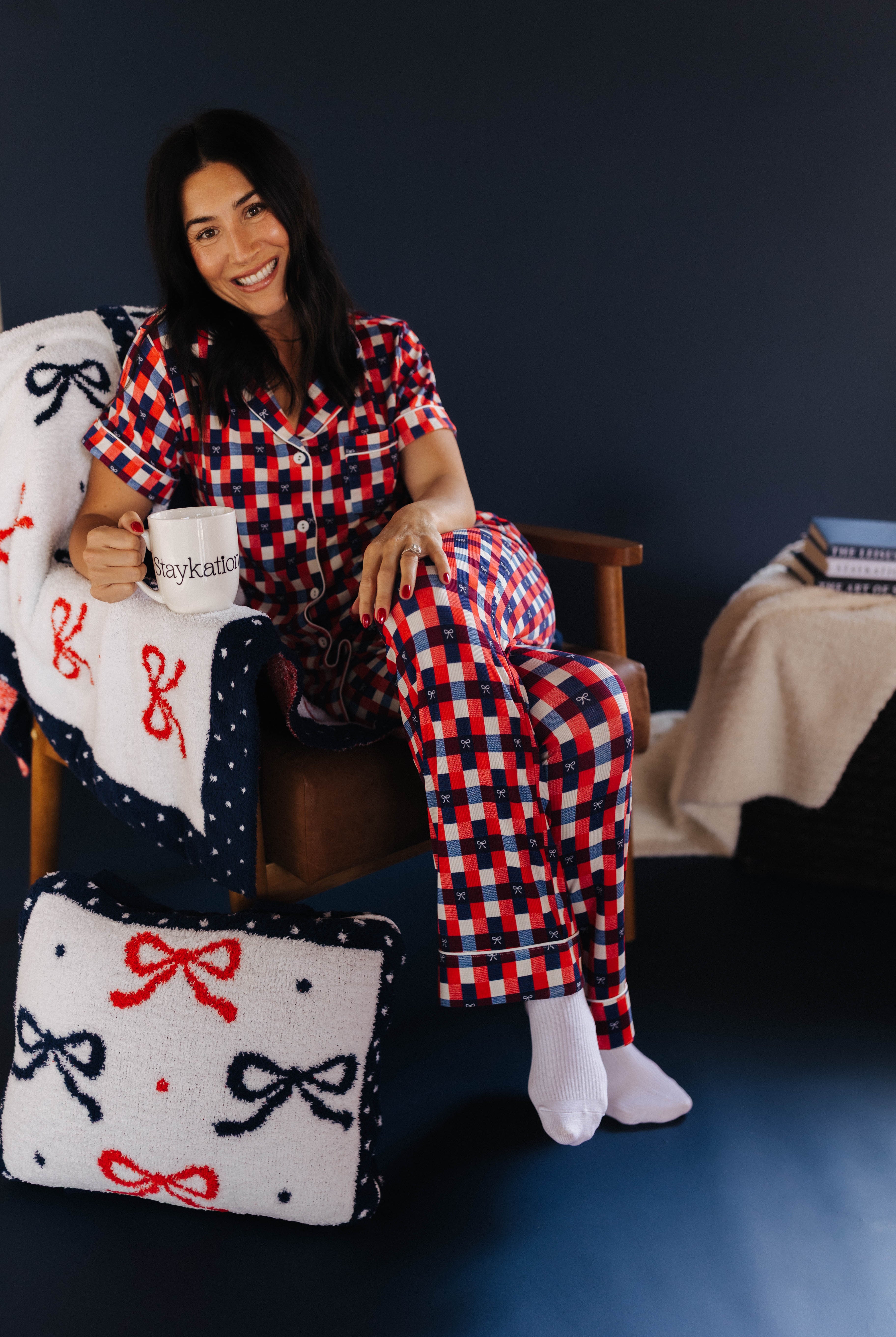 Woman in red and blue checkered pajama set sitting on a chair with a quillow featuring bows.